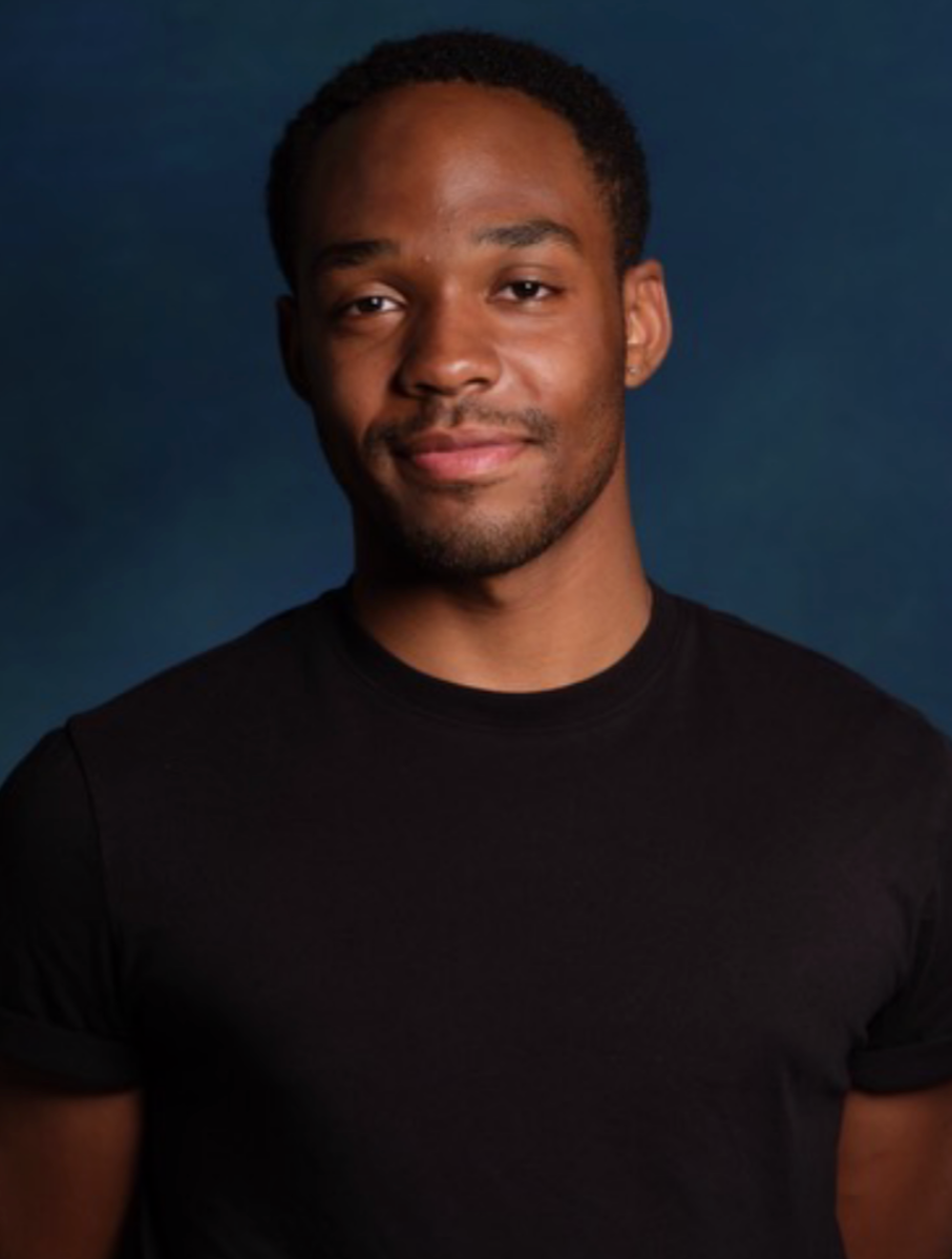 Portrait of a young man with short, curly hair, wearing a black t-shirt, against a dark blue background.