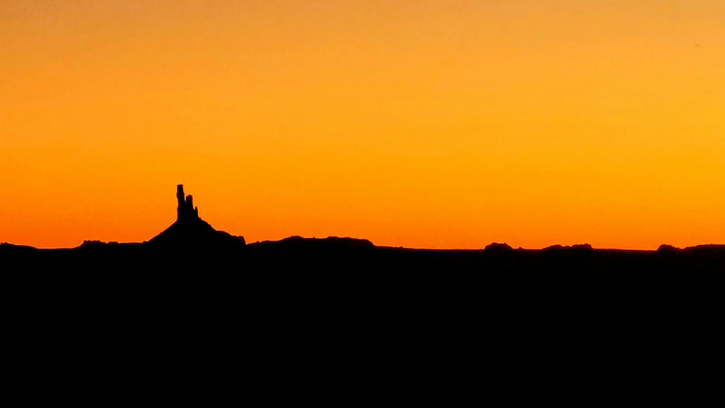 Sunset over a desert landscape with a tall rock formation in the foreground.
