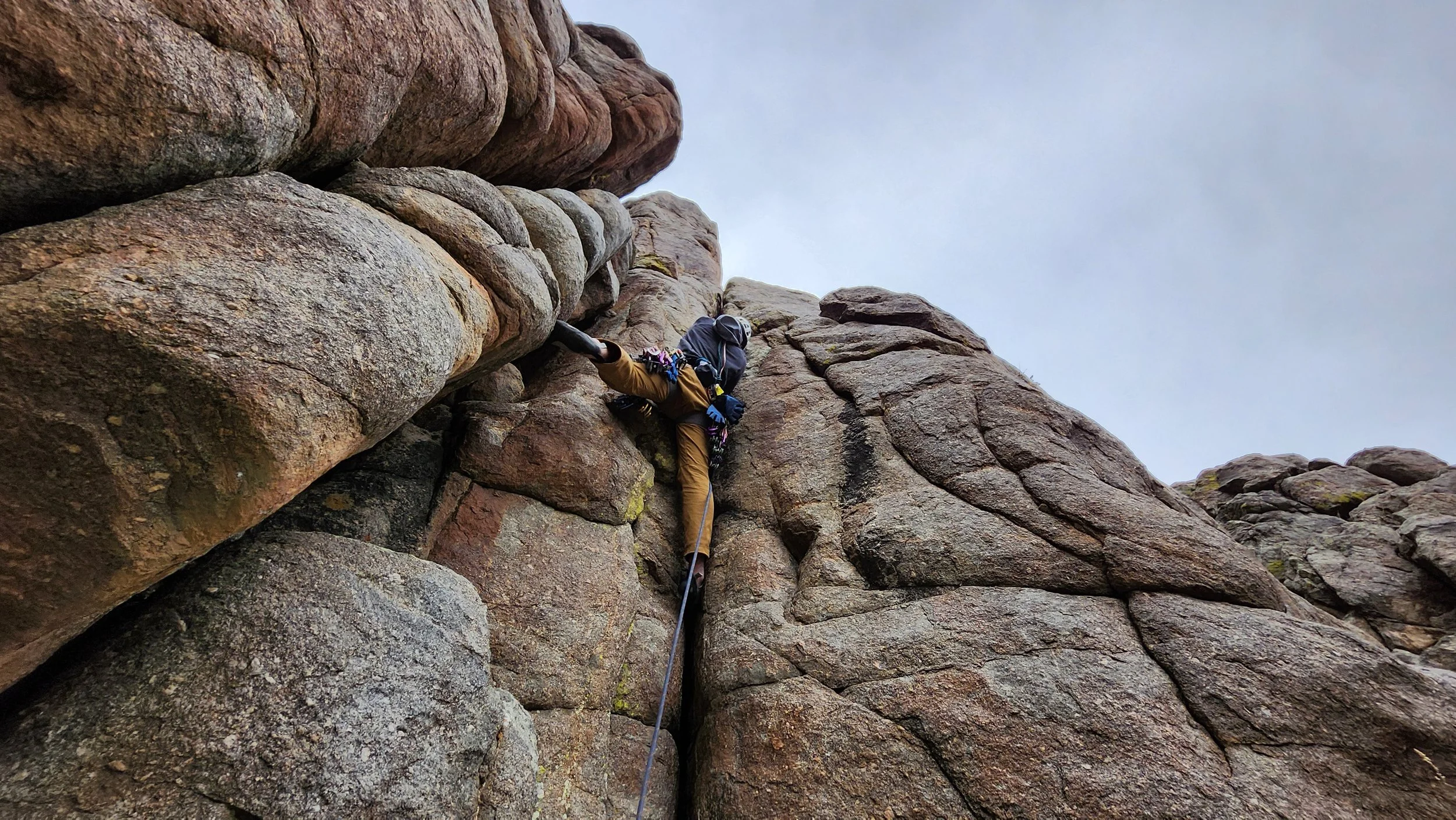 A person rock climbing on a rugged rocky cliff, wearing a helmet, harness, and outdoor gear, with a question mark over the scene.
