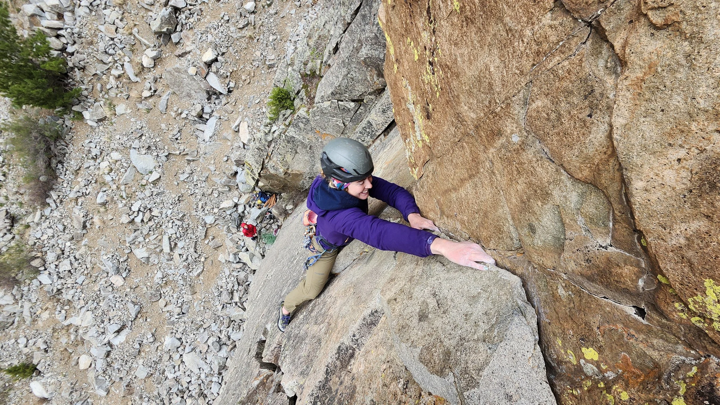 A woman with a helmet rock climbing on a steep rock face in an outdoor mountainous area.
