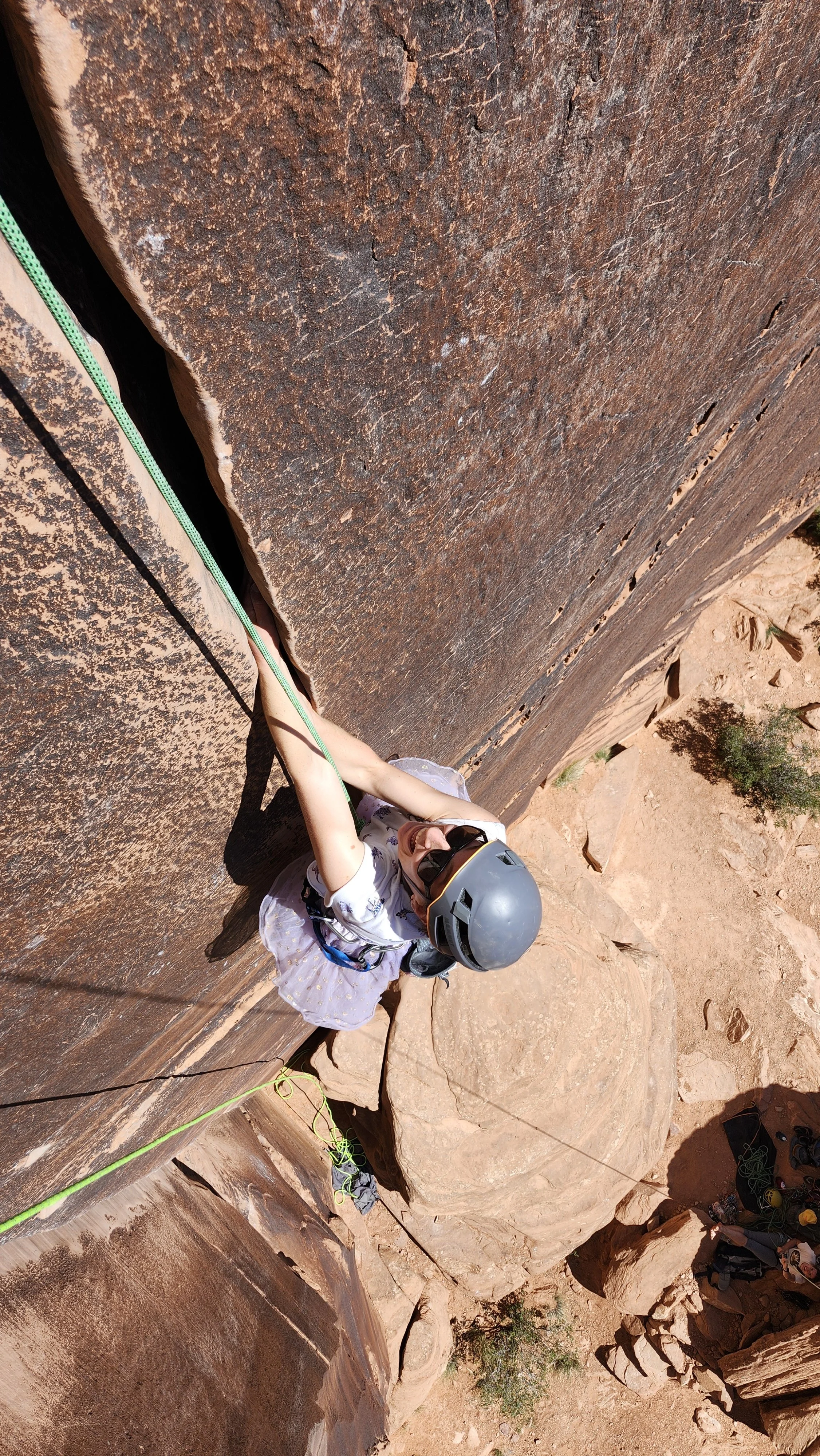 A young girl rock climbing on a vertical sandstone wall, wearing a helmet and harness, with a ropes for safety in a desert landscape.