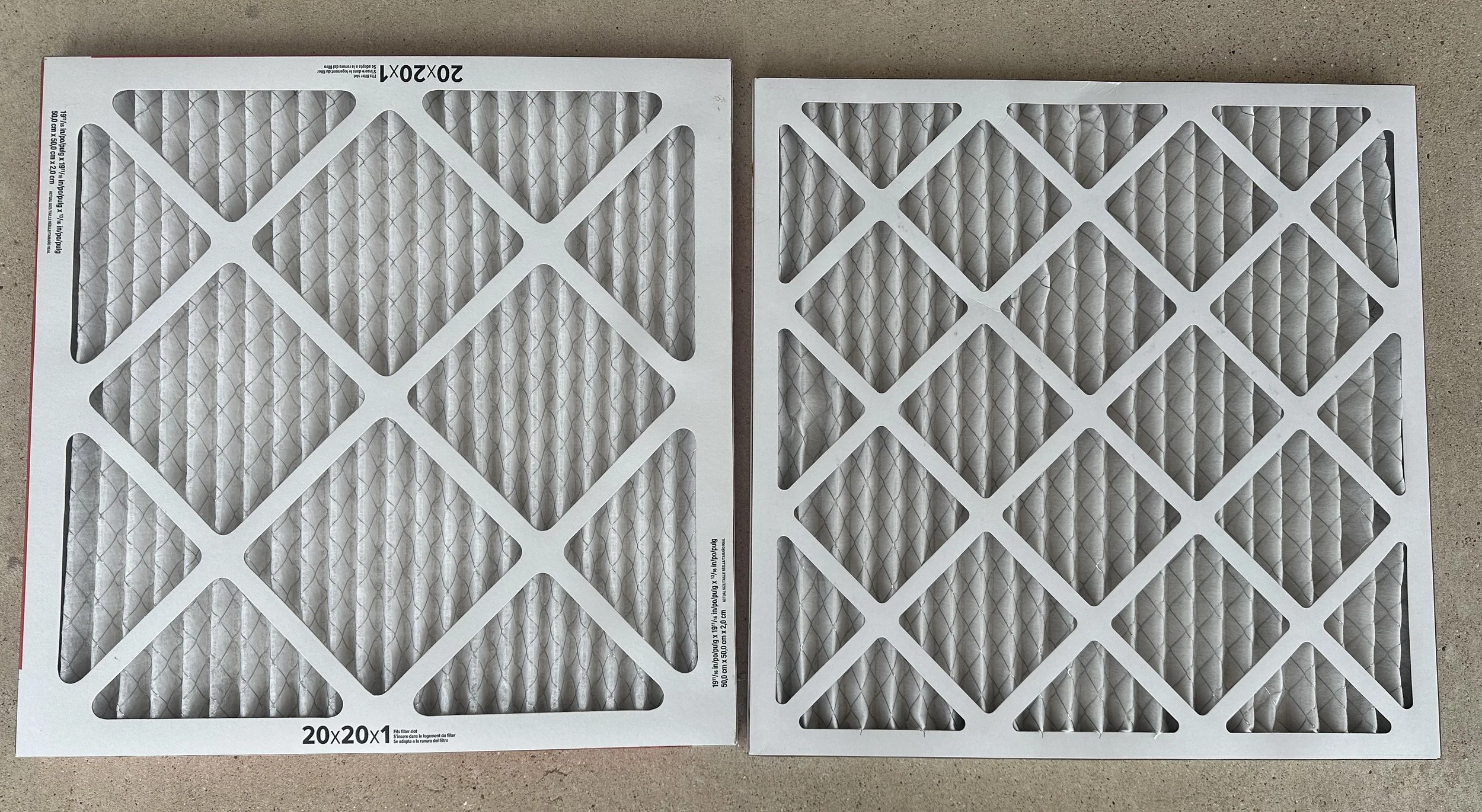 Two rectangular air filters side by side on a flat surface, with white frames and pleated filter material inside.