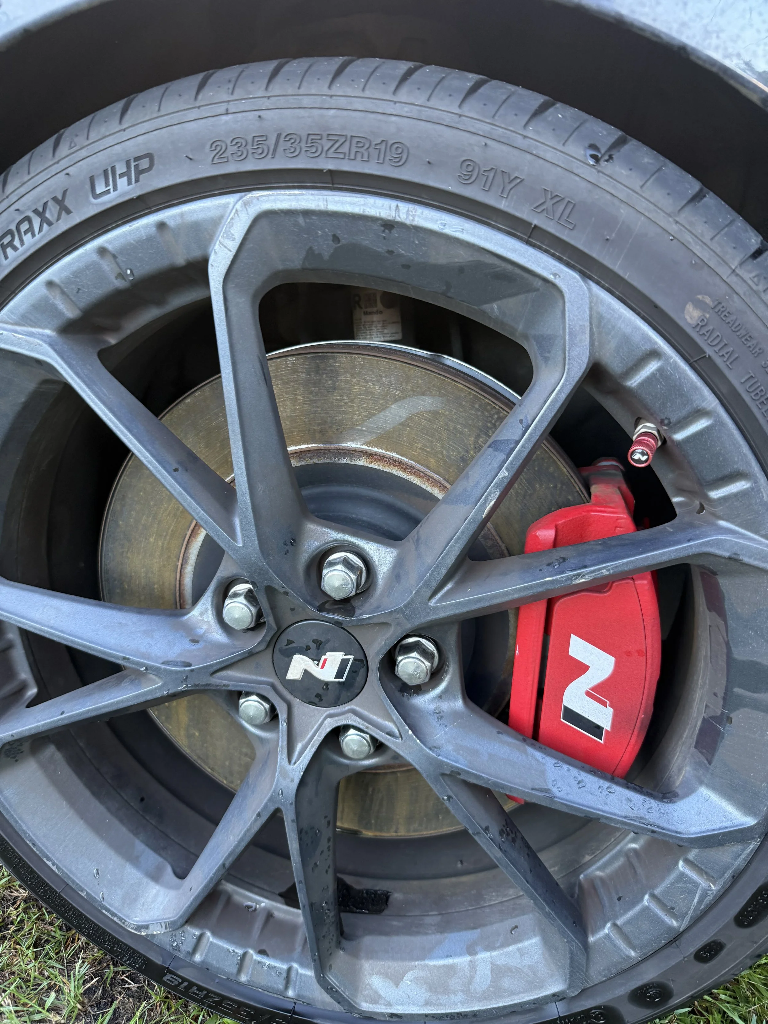Close-up of a car wheel with a yellow brake disc, a silver alloy rim with an NTT logo in the center, and a red brake caliper.