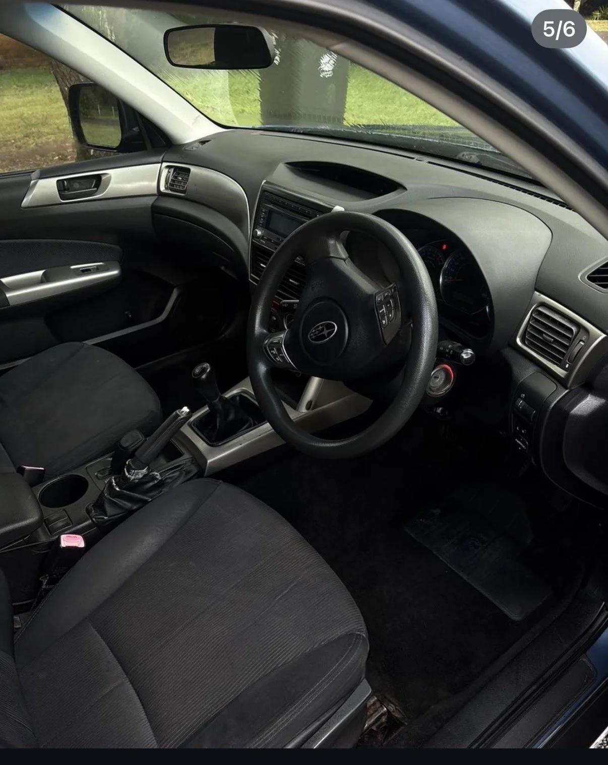 Inside view of a Toyota car's driver's side, showing the steering wheel, dashboard, center console, gear shift, and front seats. The interior is black and gray with some controls and vents visible.
