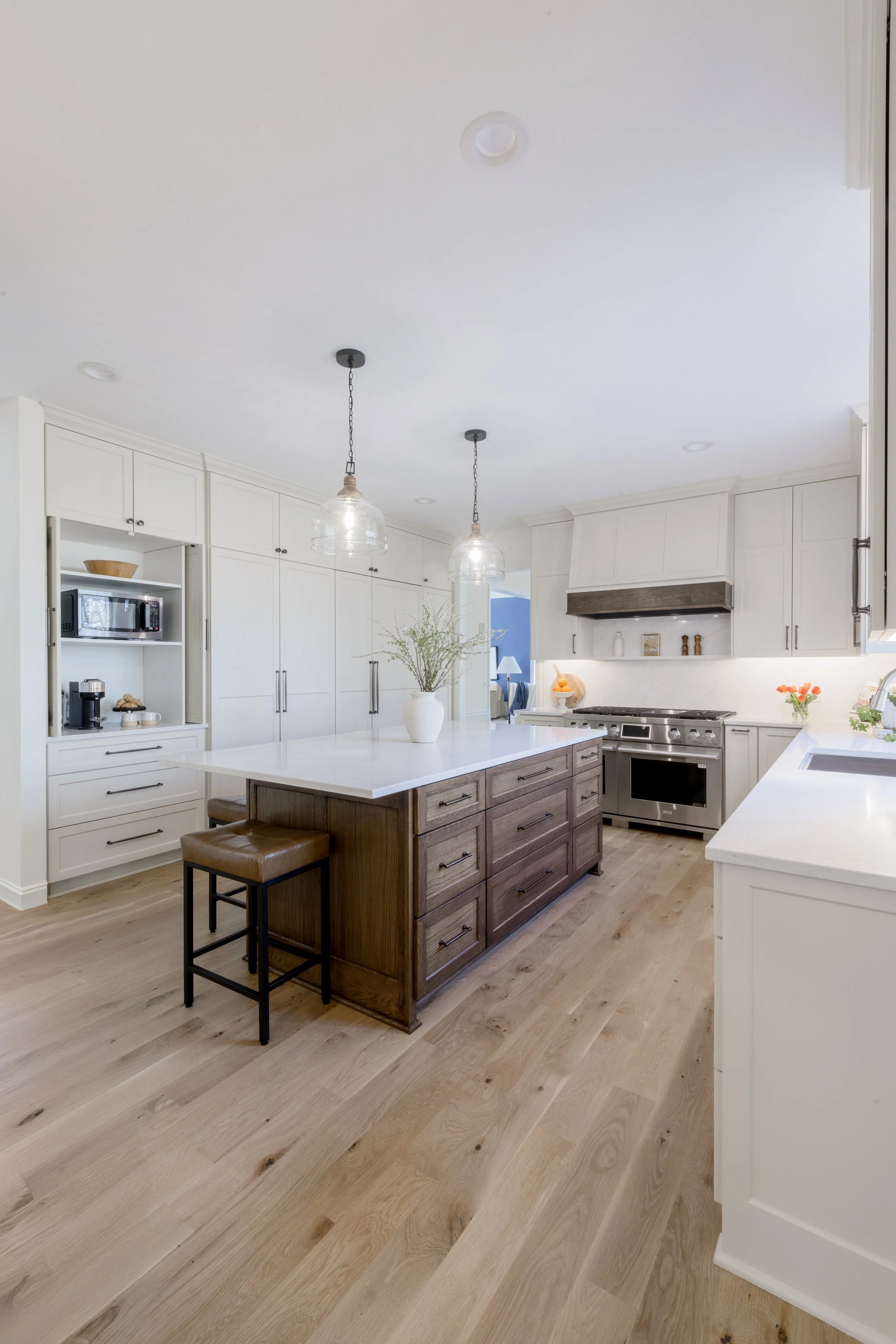 Clean, modern kitchen with white cabinets, a kitchen island with dark wood finish, two pendant lights, stainless steel oven, and hardwood flooring.
