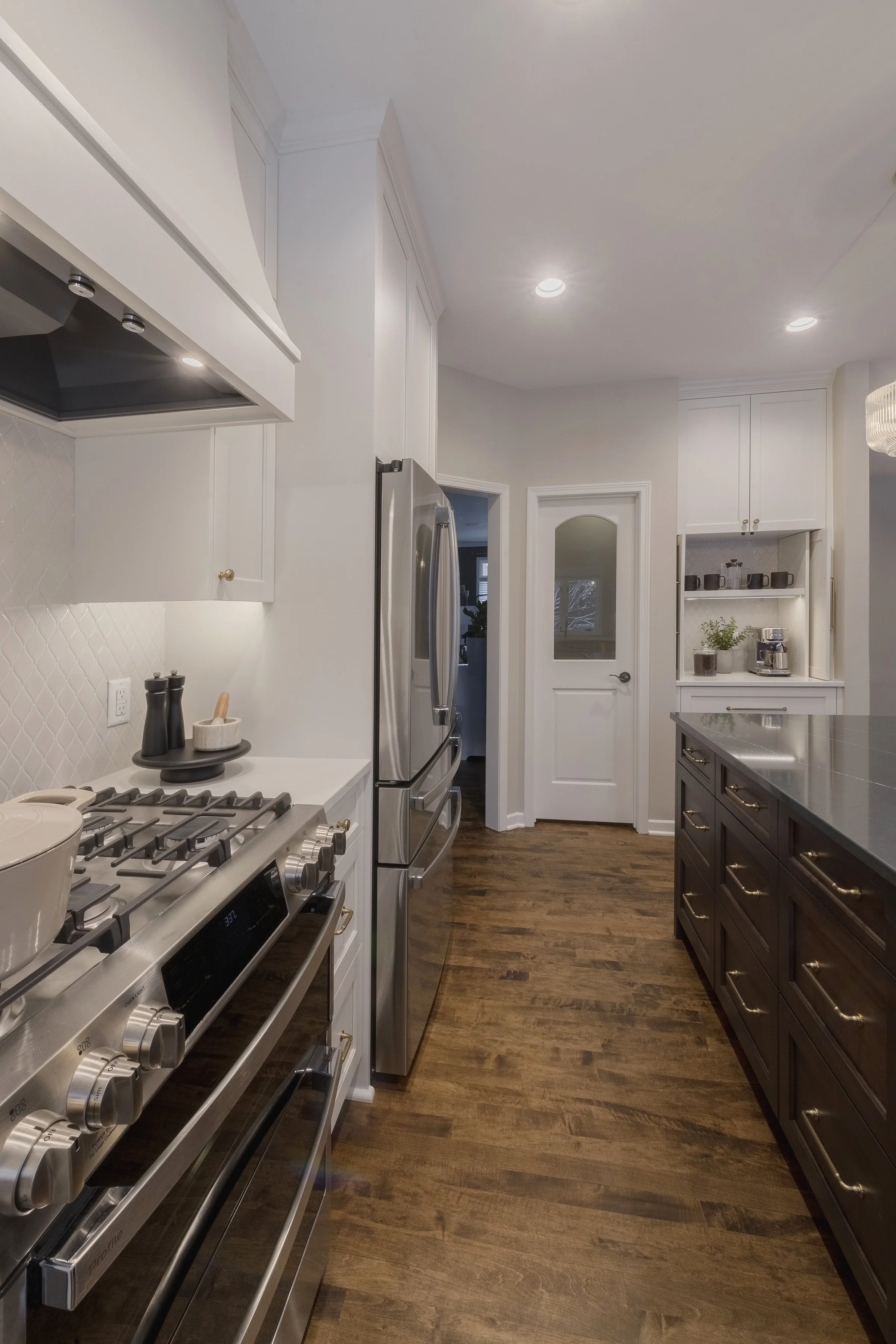 Modern kitchen with stainless steel appliances, white upper cabinets, dark lower cabinets, hardwood floors, and a white door with a frosted glass panel.