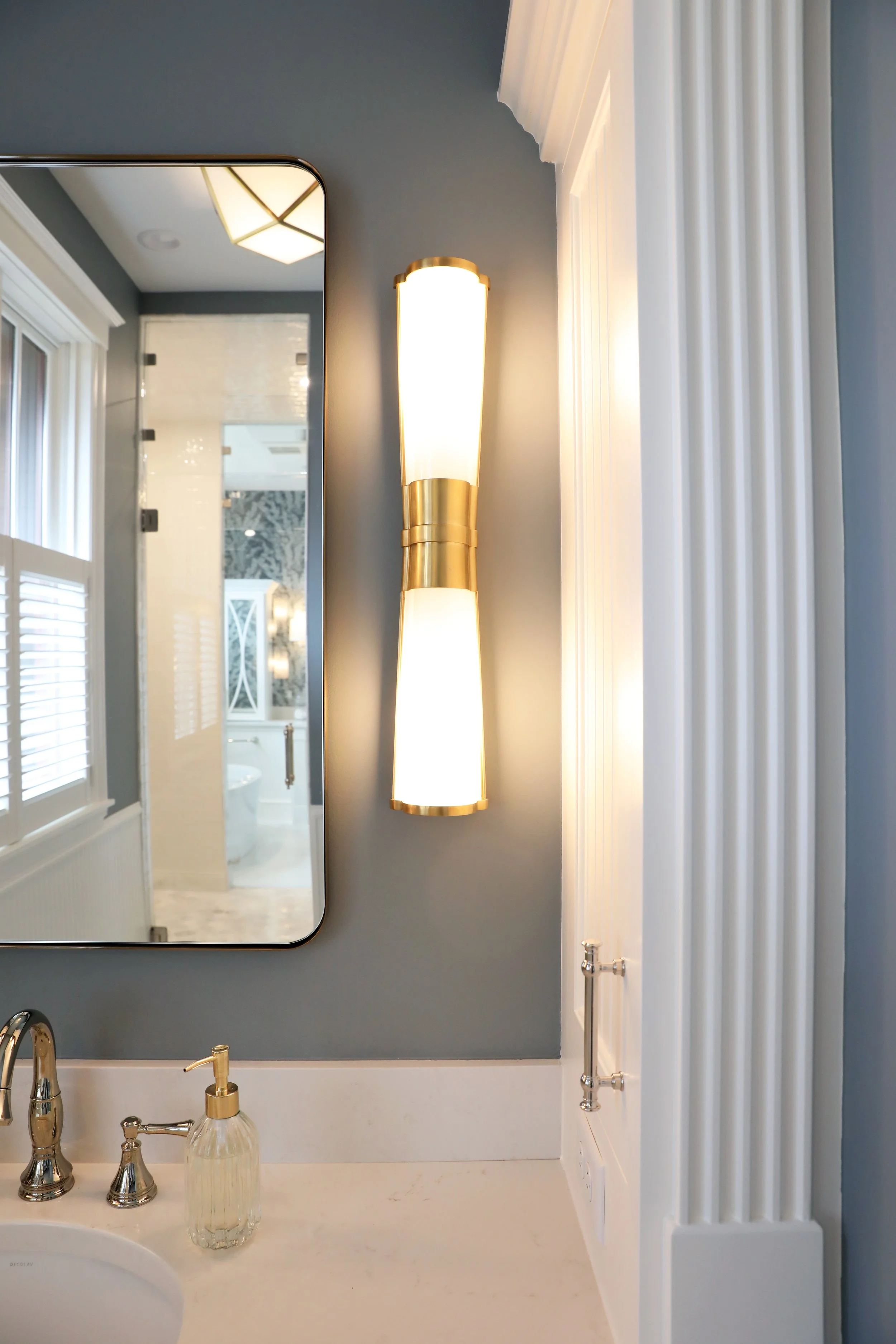 Bathroom with a white countertop, gold fixtures, a mirror, and a modern wall-mounted light fixture.
