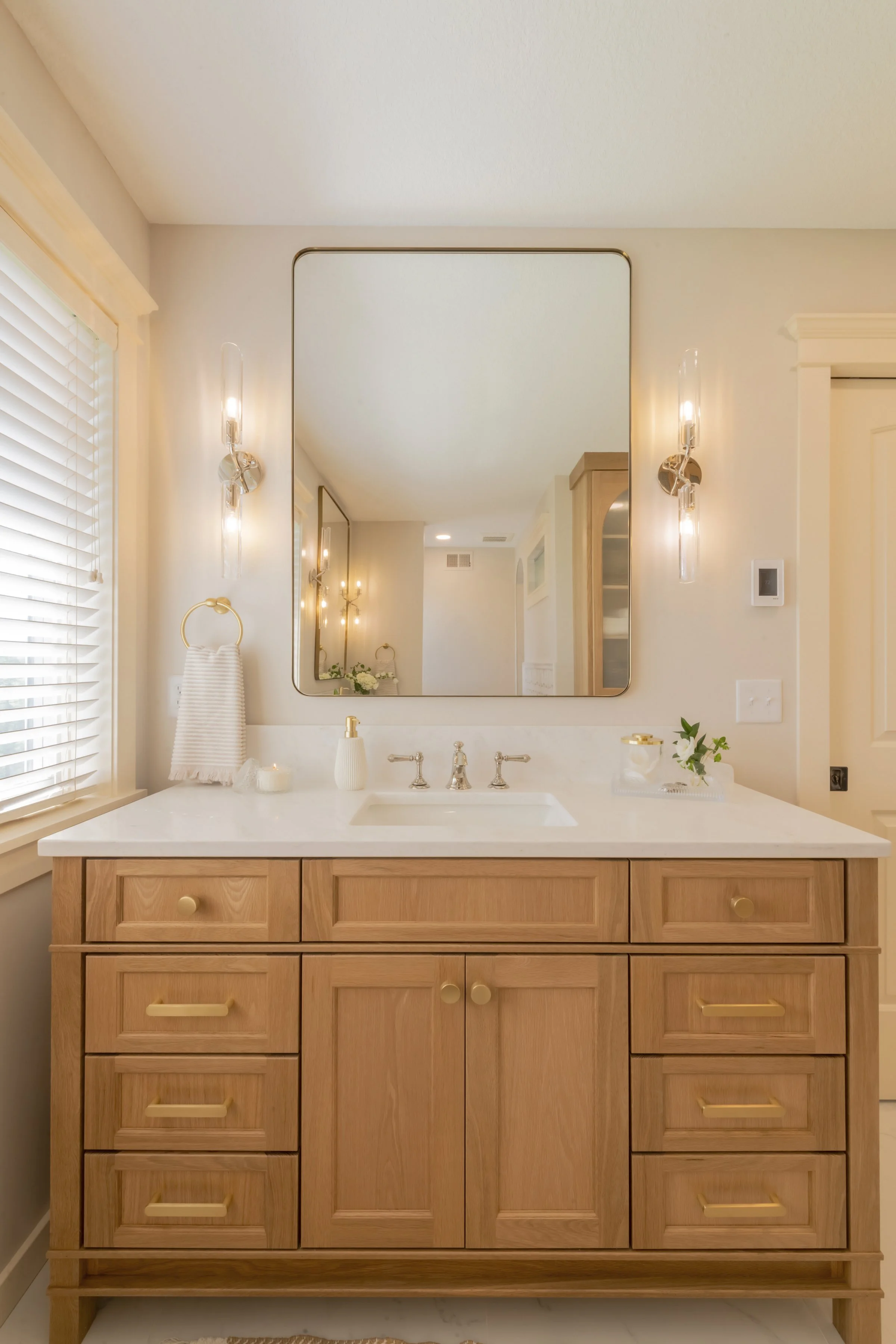 A bathroom vanity with a wooden cabinet, white countertop, and a mirror above it, flanked by two wall-mounted lights.