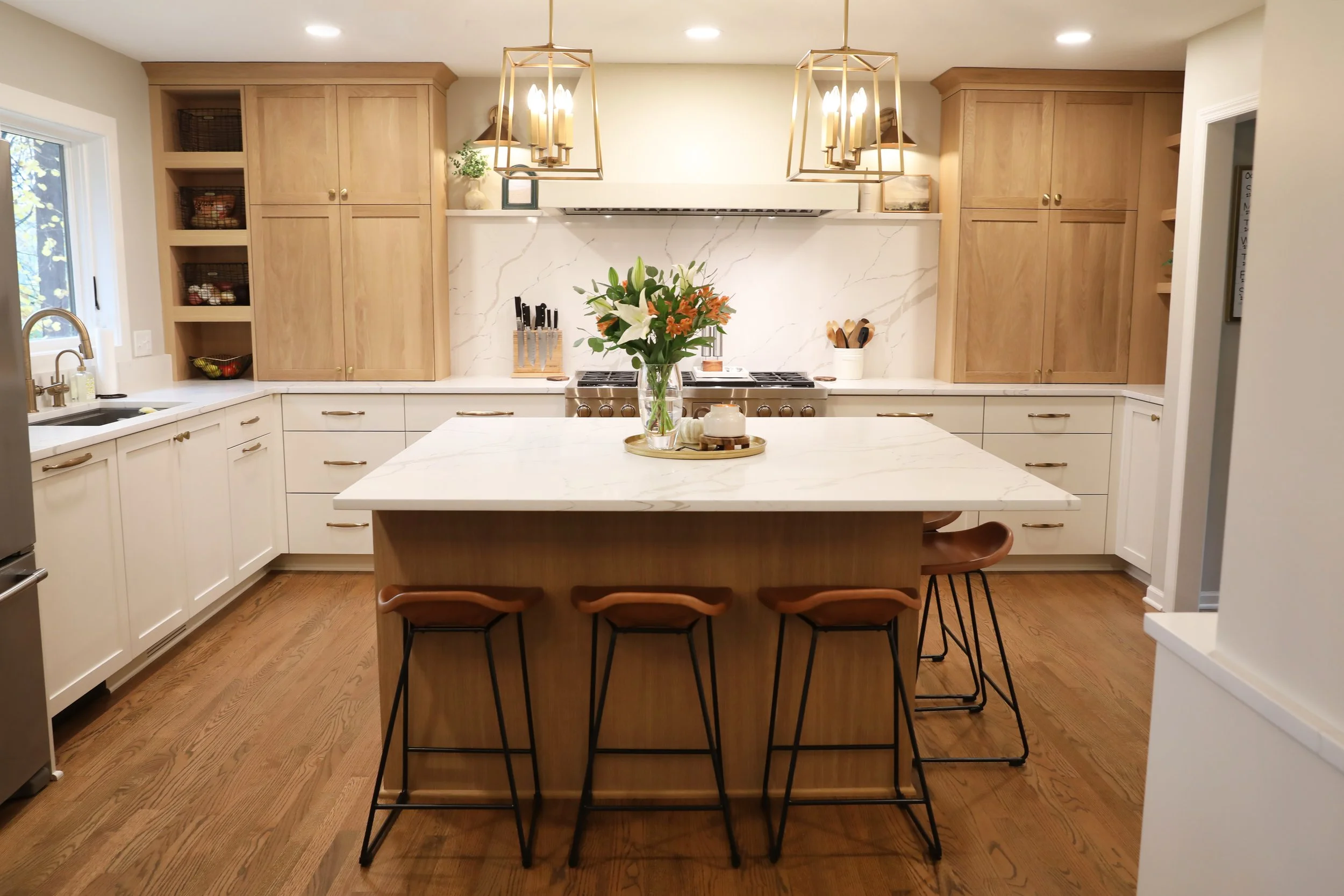 Modern kitchen with white and wood cabinetry, marble backsplash, wooden dining table with chairs, and decorative lighting fixtures.