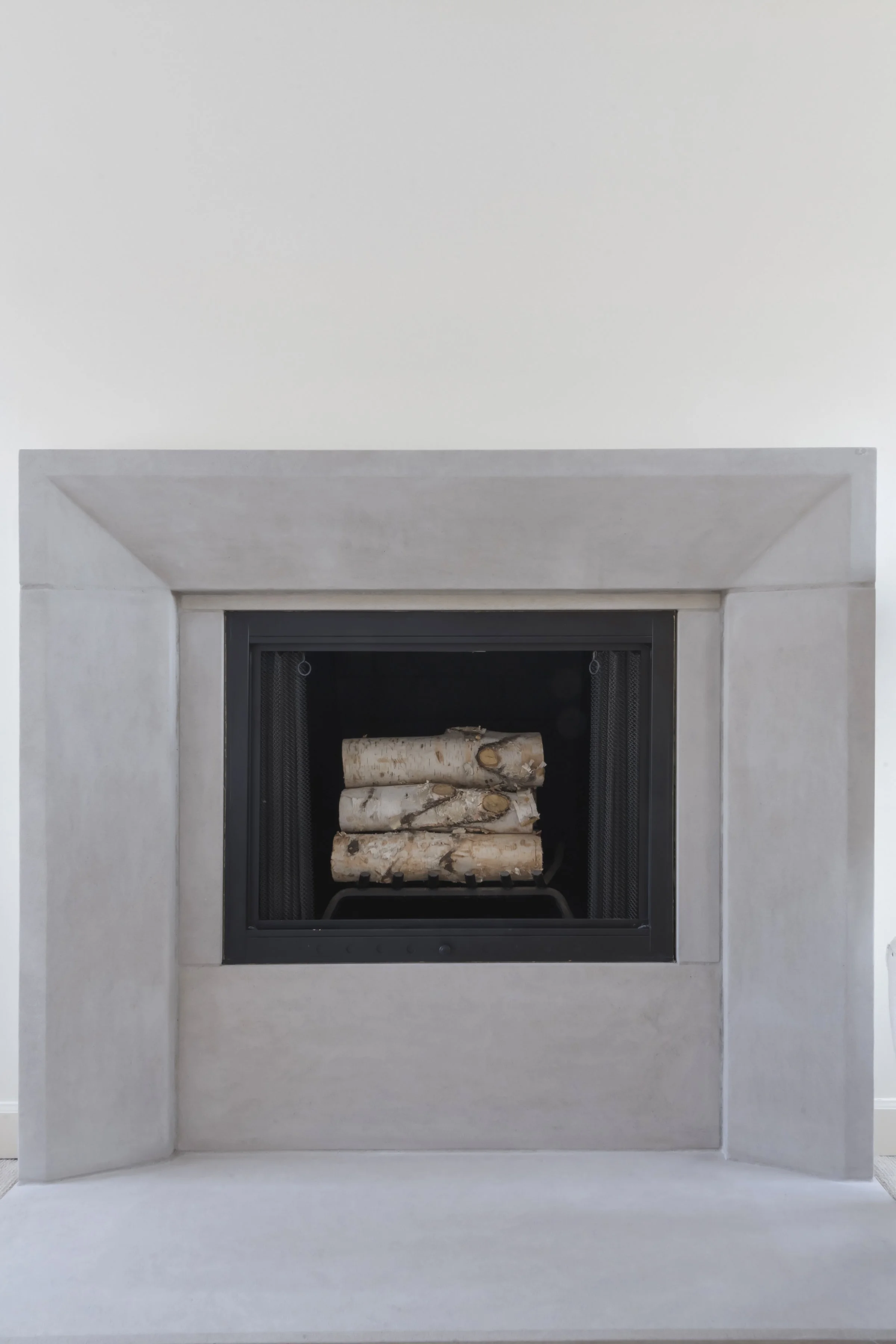 White fireplace with a black interior, stacked with firewood logs inside.
