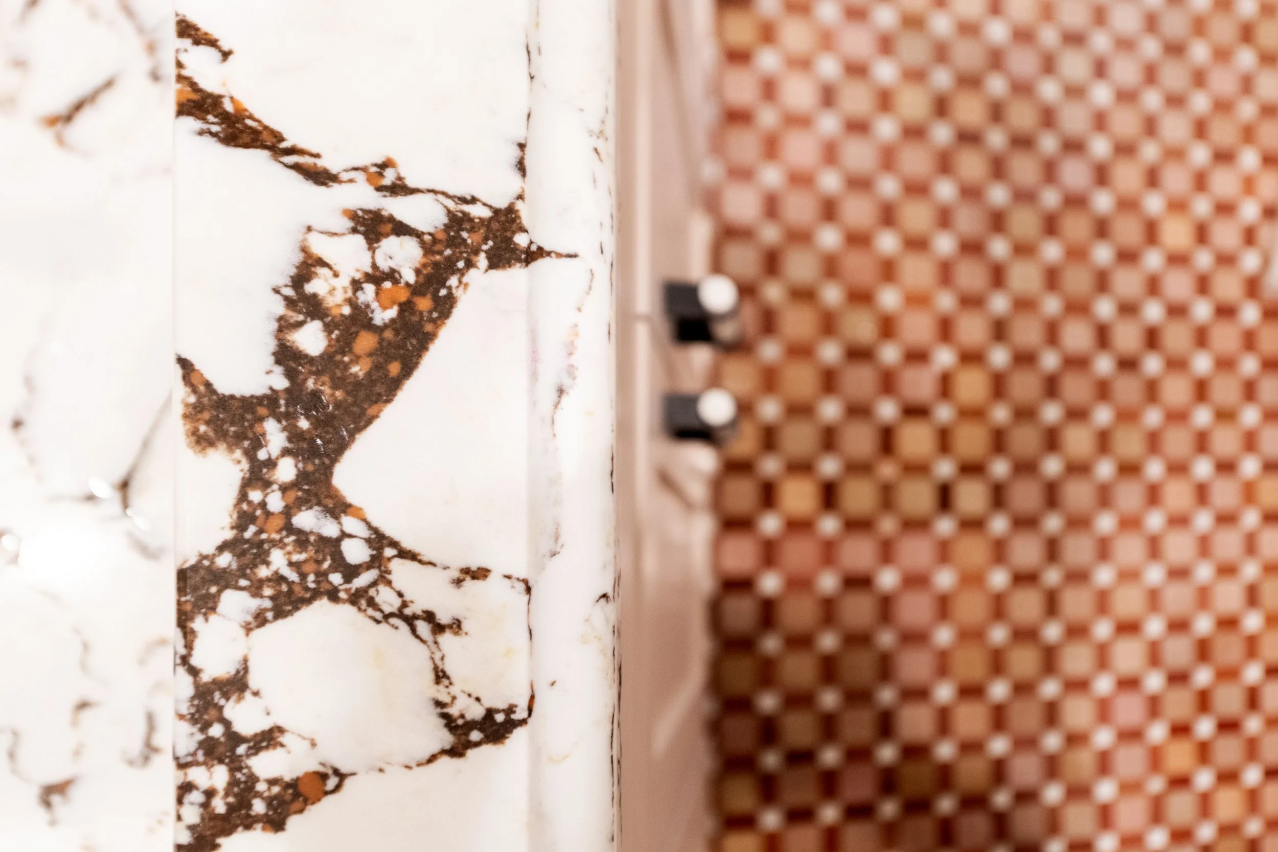 Close-up of a marble surface with brown and white veining and some orange spots, with a perforated reddish-brown tile background.