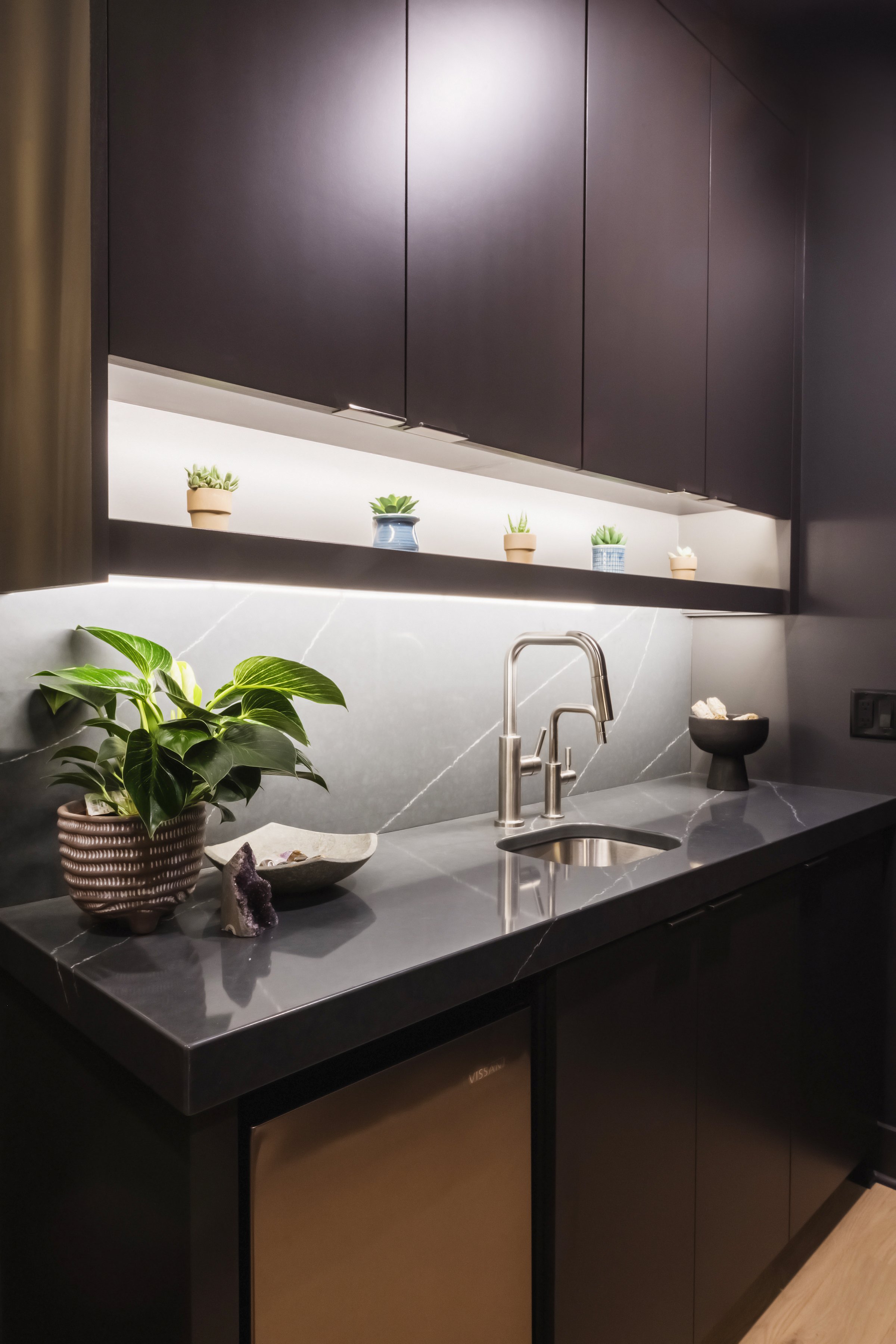 Modern kitchen with black cabinets, gray marble countertop, sink, and decorative plants in pots.