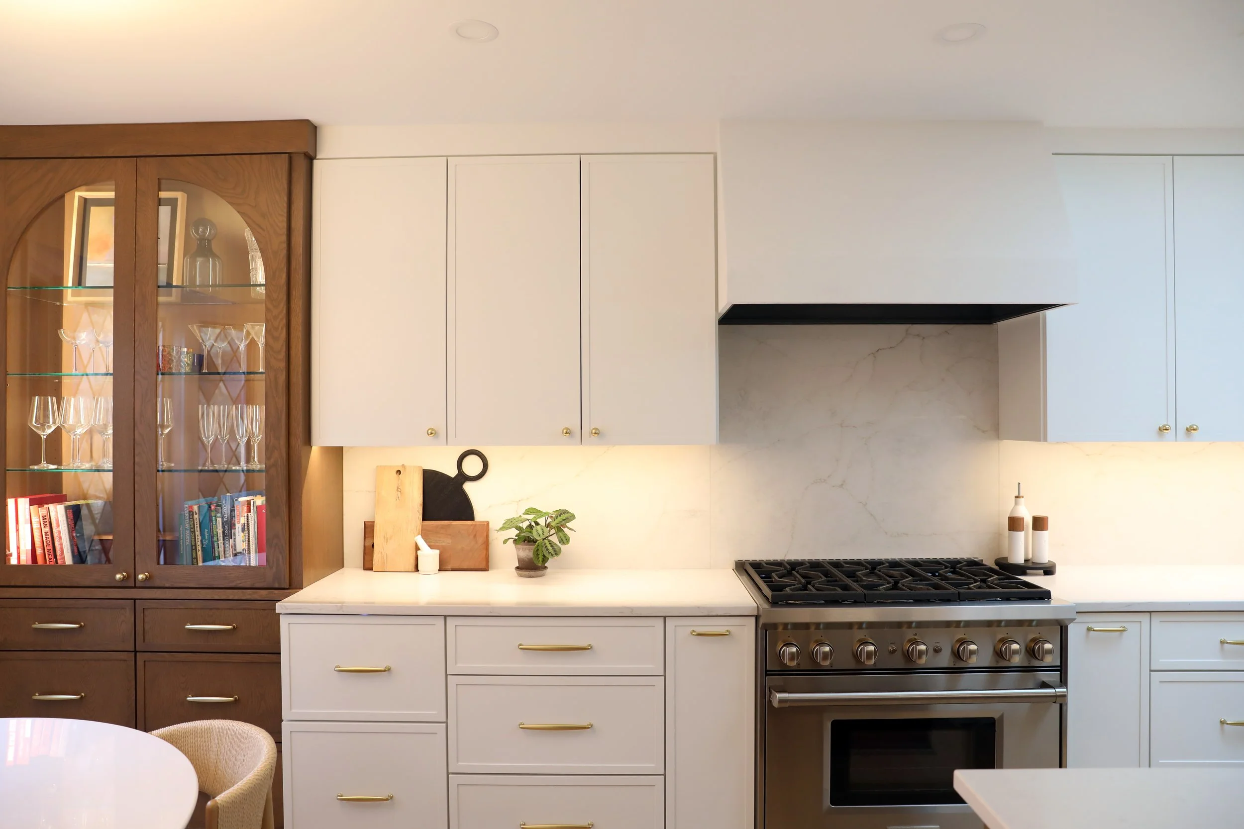 Modern kitchen with white cabinets, a black stove, and a wooden display cabinet filled with glassware and books.