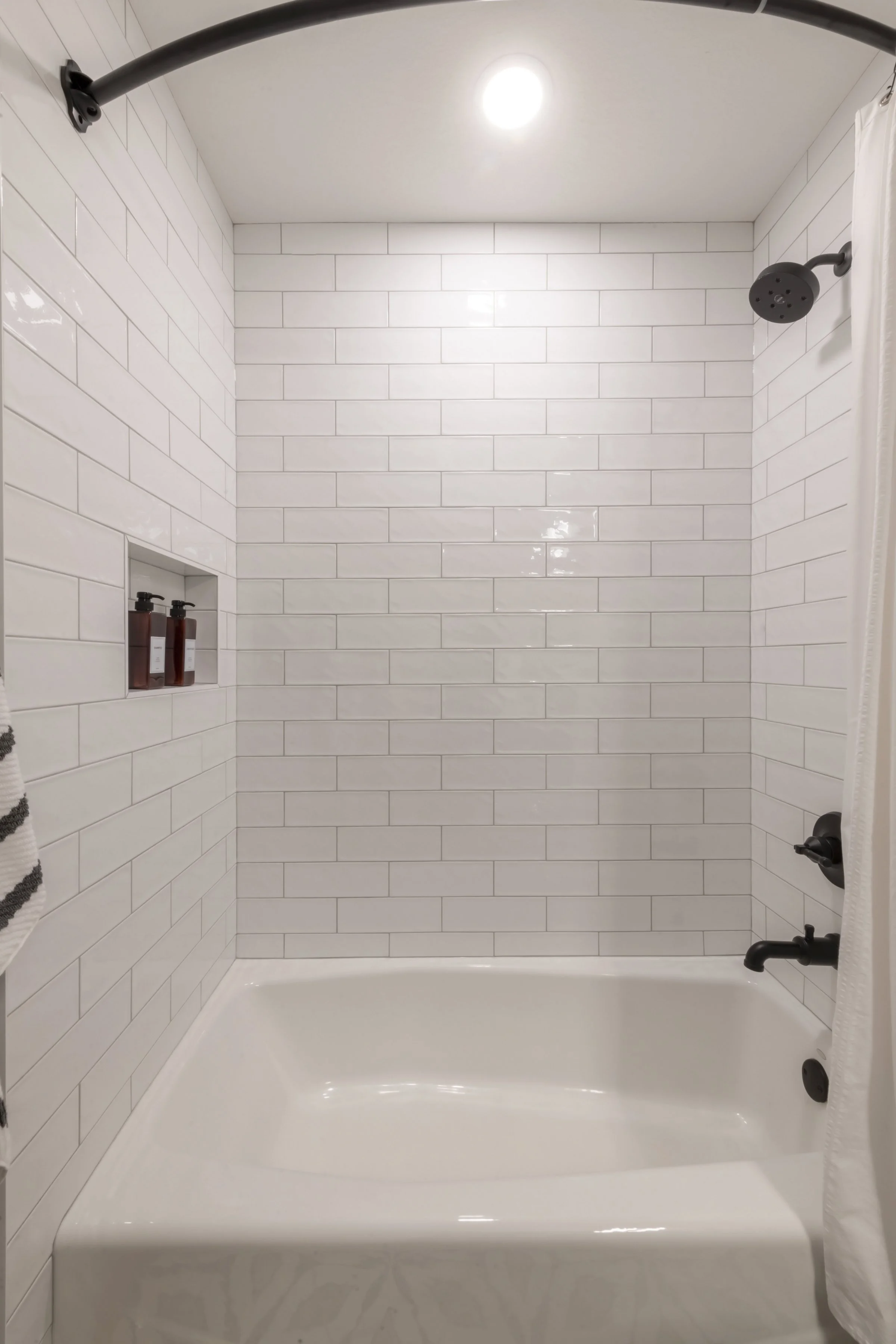 Bathroom shower with white subway tiles, black showerhead, and a white shower curtain.