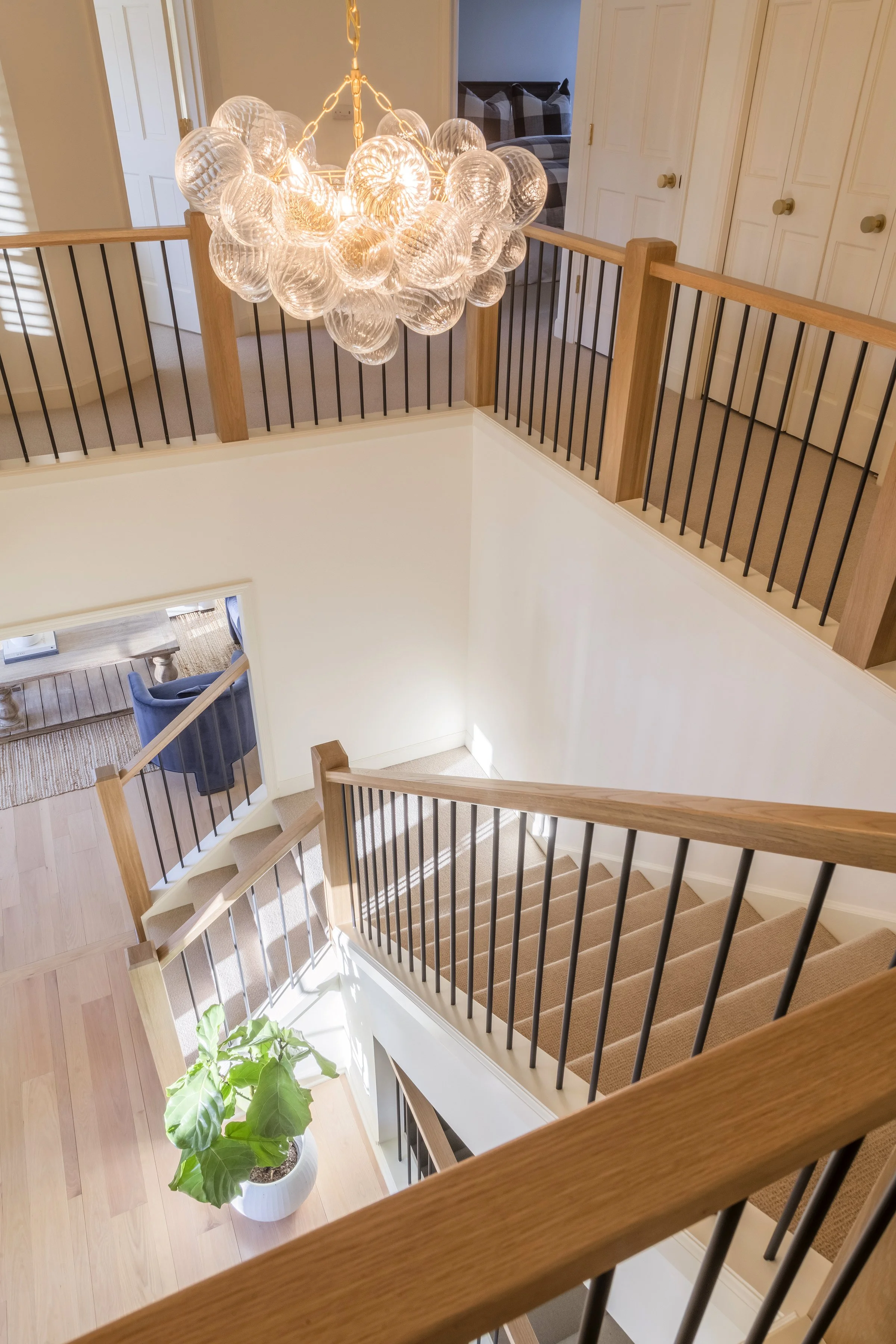 A view of a staircase landing and hallway in a home, featuring a large chandelier made of glass globes hanging from the ceiling, a potted plant with large green leaves, and multiple doors with round knobs.