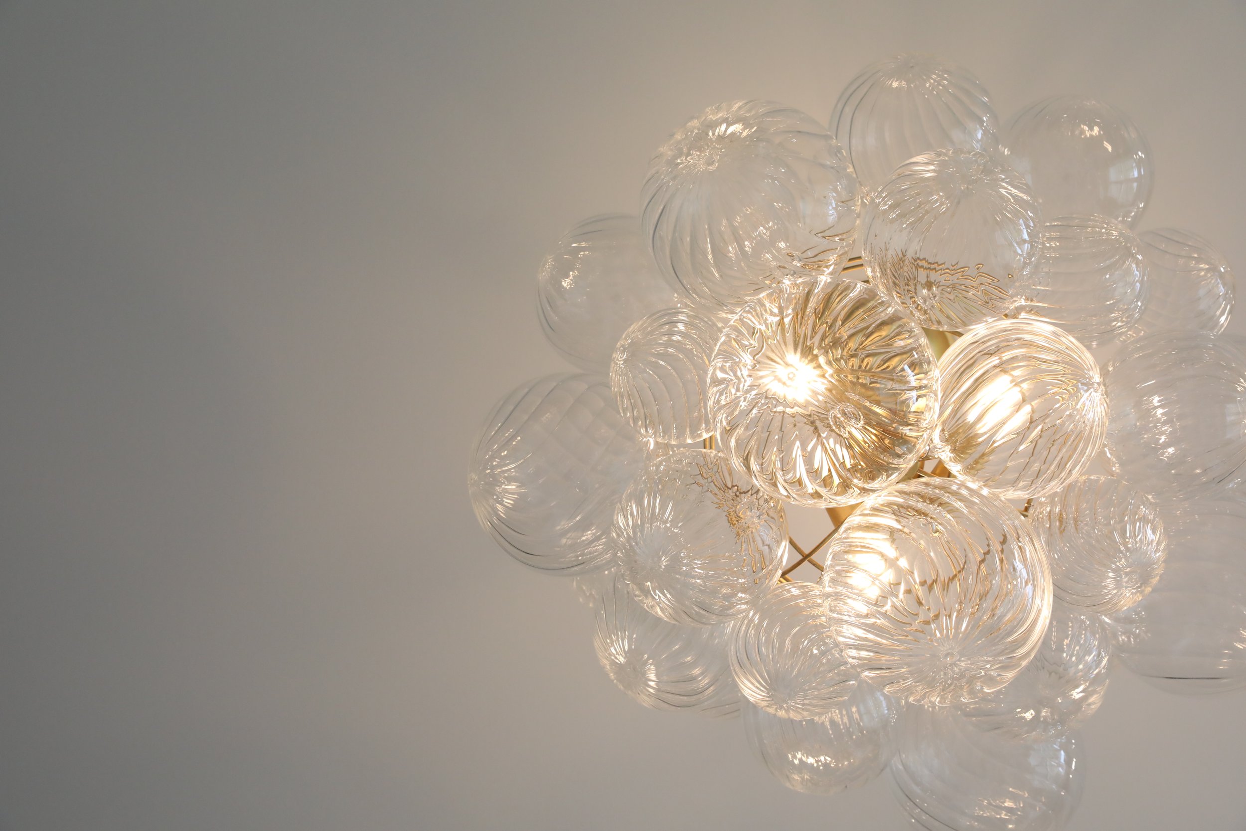 A cluster of clear glass spherical light fixtures with intricate spiral patterns, illuminated and hanging from the ceiling.