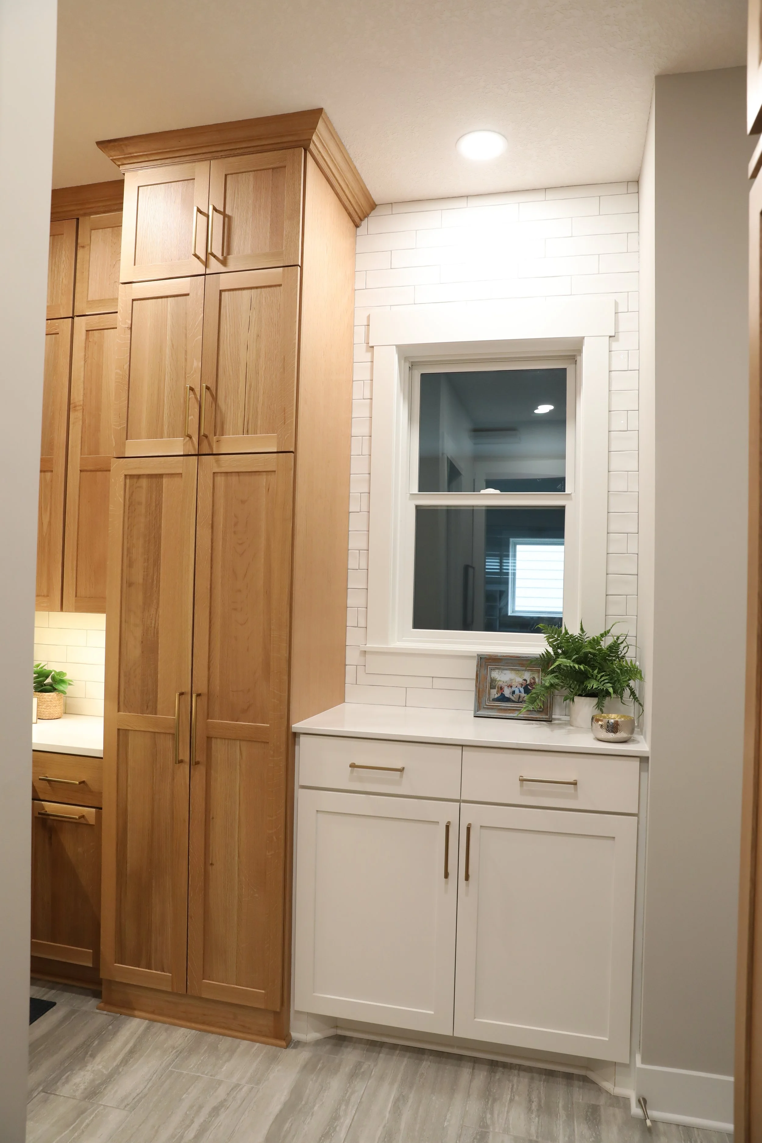 A kitchen corner with wooden and white cabinetry, a window, and decorative items including a framed photo and potted fern plant.