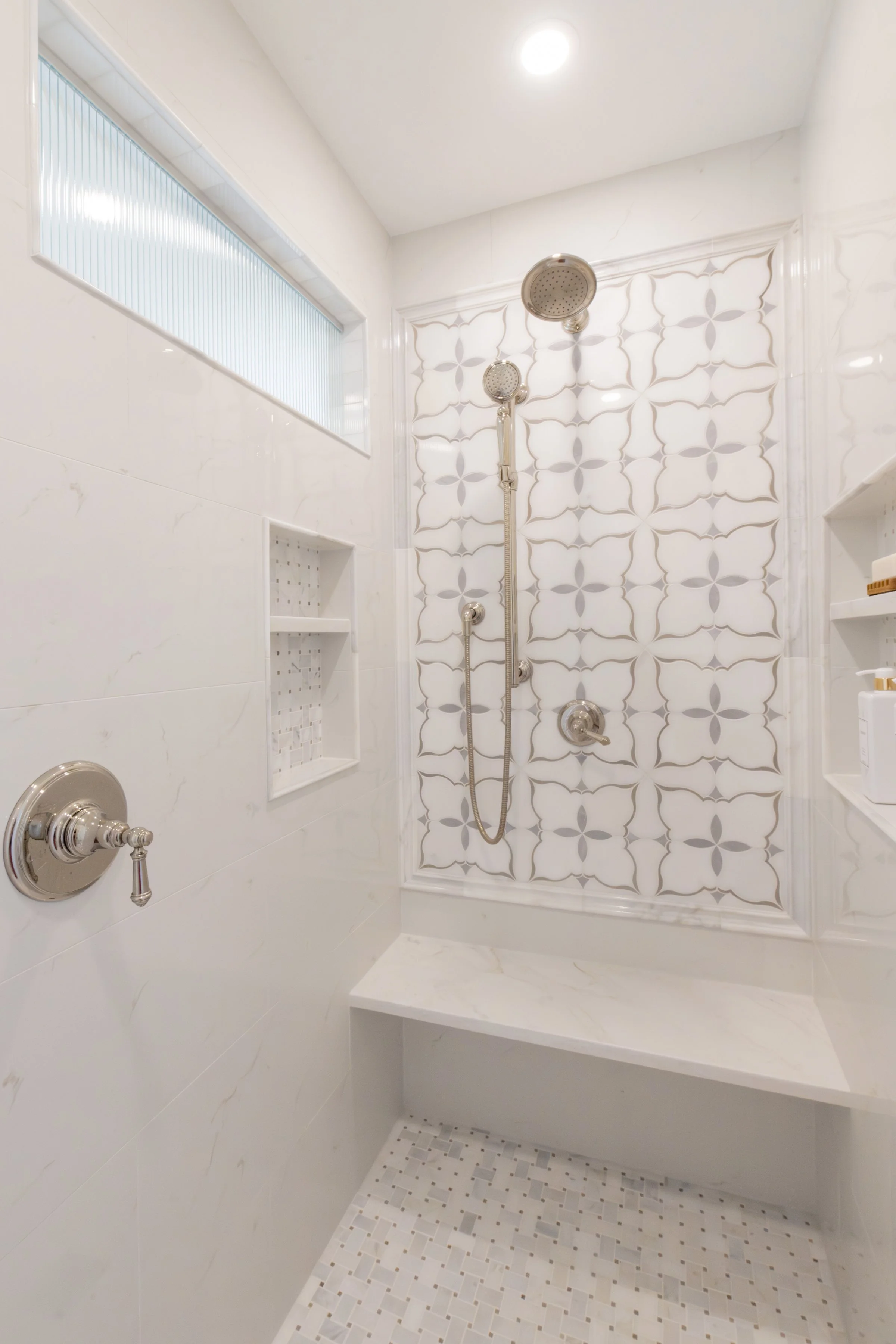 Modern walk-in shower with decorative tiled wall, built-in niche, and a frosted window for privacy