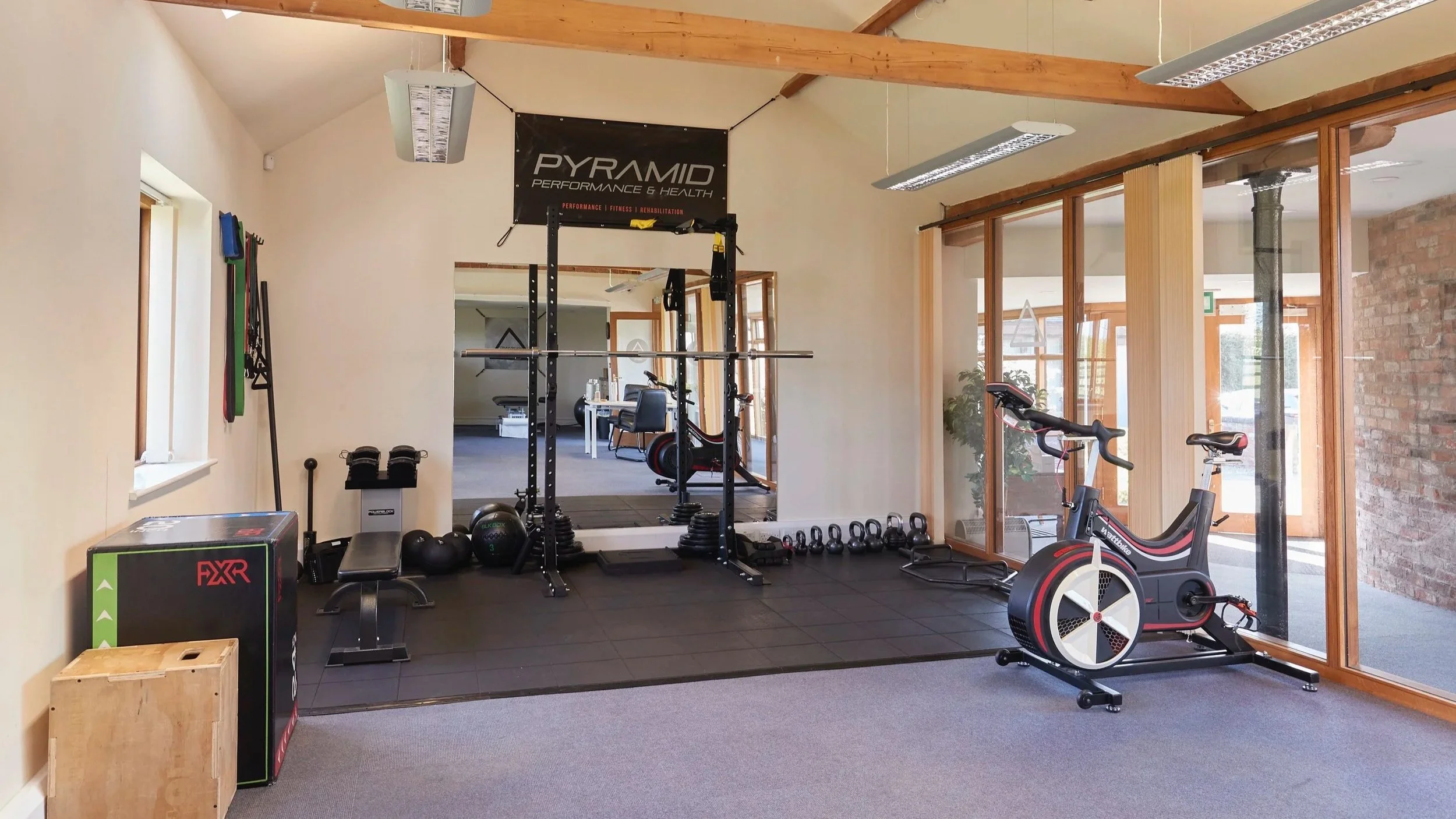 Fitness gym with weightlifting equipment, a rowing machine, kettlebells, medicine balls, resistance bands, and a banner that reads 'PYRAMID Performance & Health'.