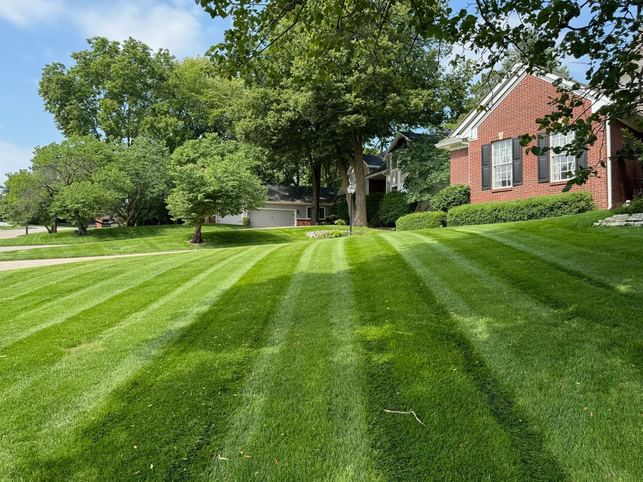 Well-maintained front lawn with striped green grass, trees, and a red brick house in the background.