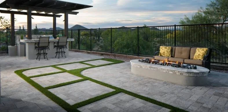 Outdoor patio with a seating area, a fire pit, barstools, a table under a shade structure, and a landscape view of trees and mountains in the distance.