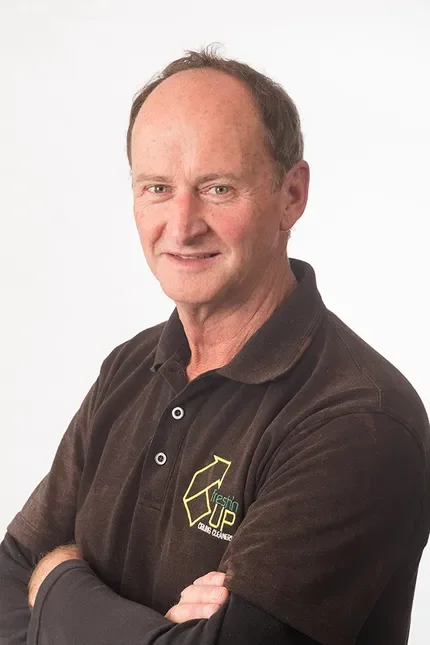 Portrait of a middle-aged man with short hair, wearing a dark polo shirt with a logo on it, standing against a plain white background.