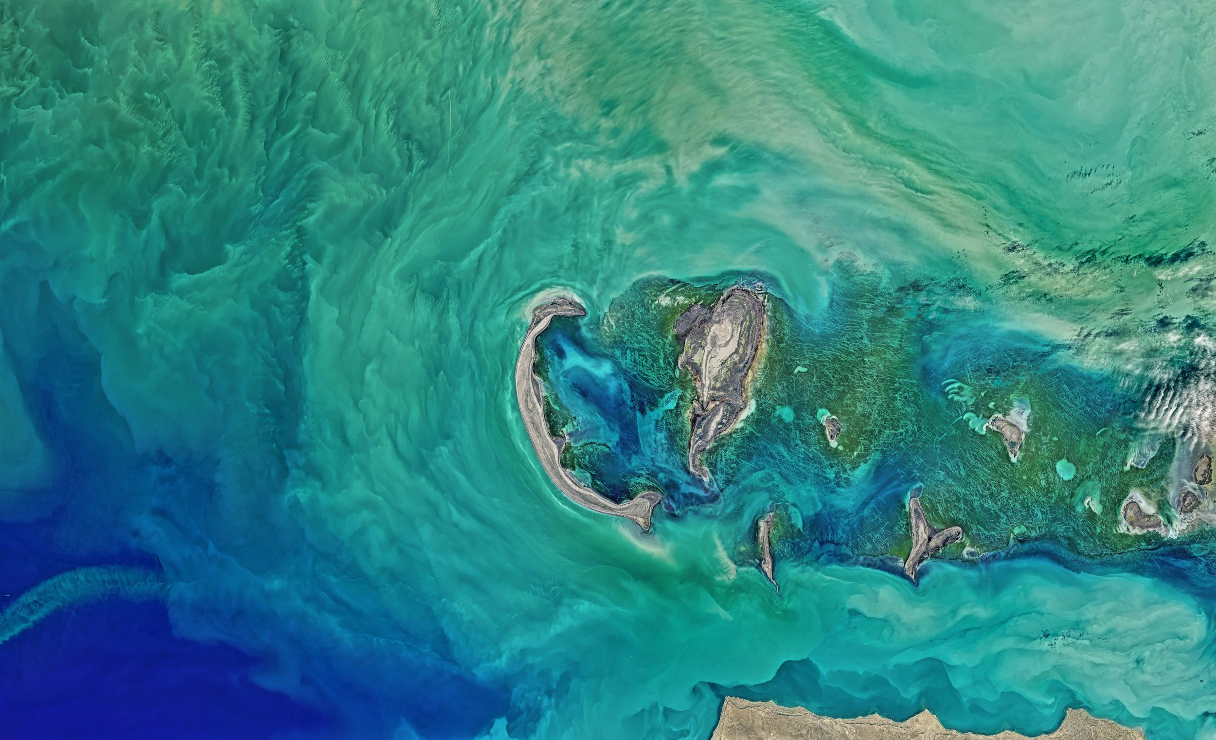 Una vista aérea de una isla tropical rodeada de aguas turquesas, con arrecifes de coral y algunas islas más pequeñas en las cercanías.