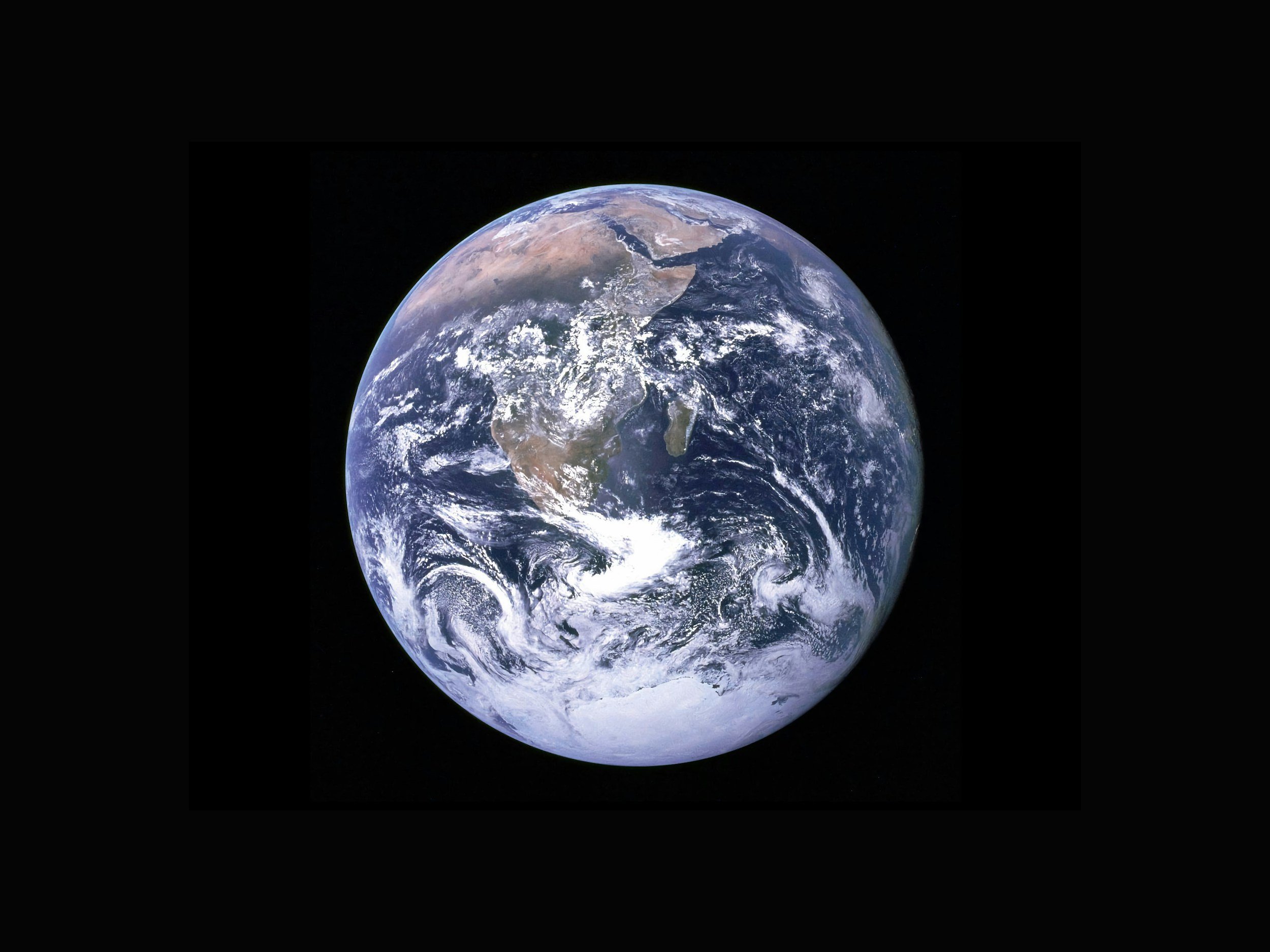 Fotografía de la Tierra tomada desde el espacio, en la que se aprecian los continentes, los océanos, la capa de nubes y la atmósfera sobre el fondo negro del espacio.