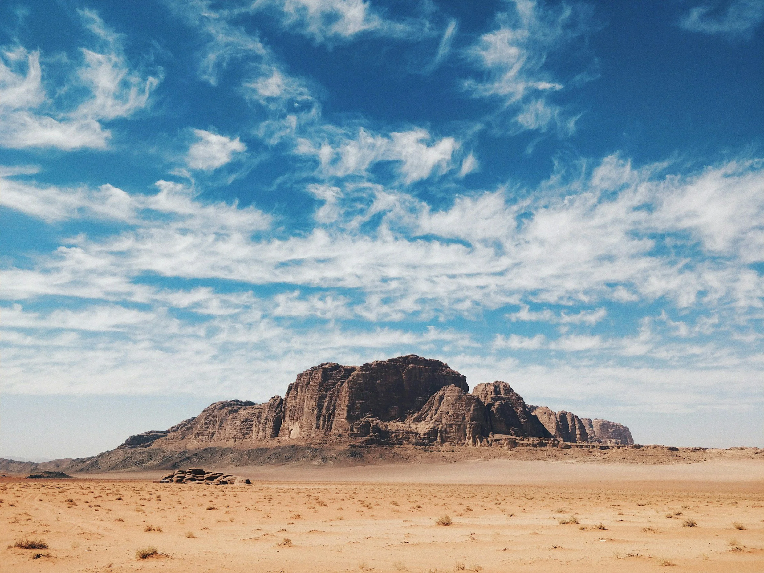 Un paisaje desértico con una gran formación rocosa, con un cielo azul salpicado de nubes blancas.