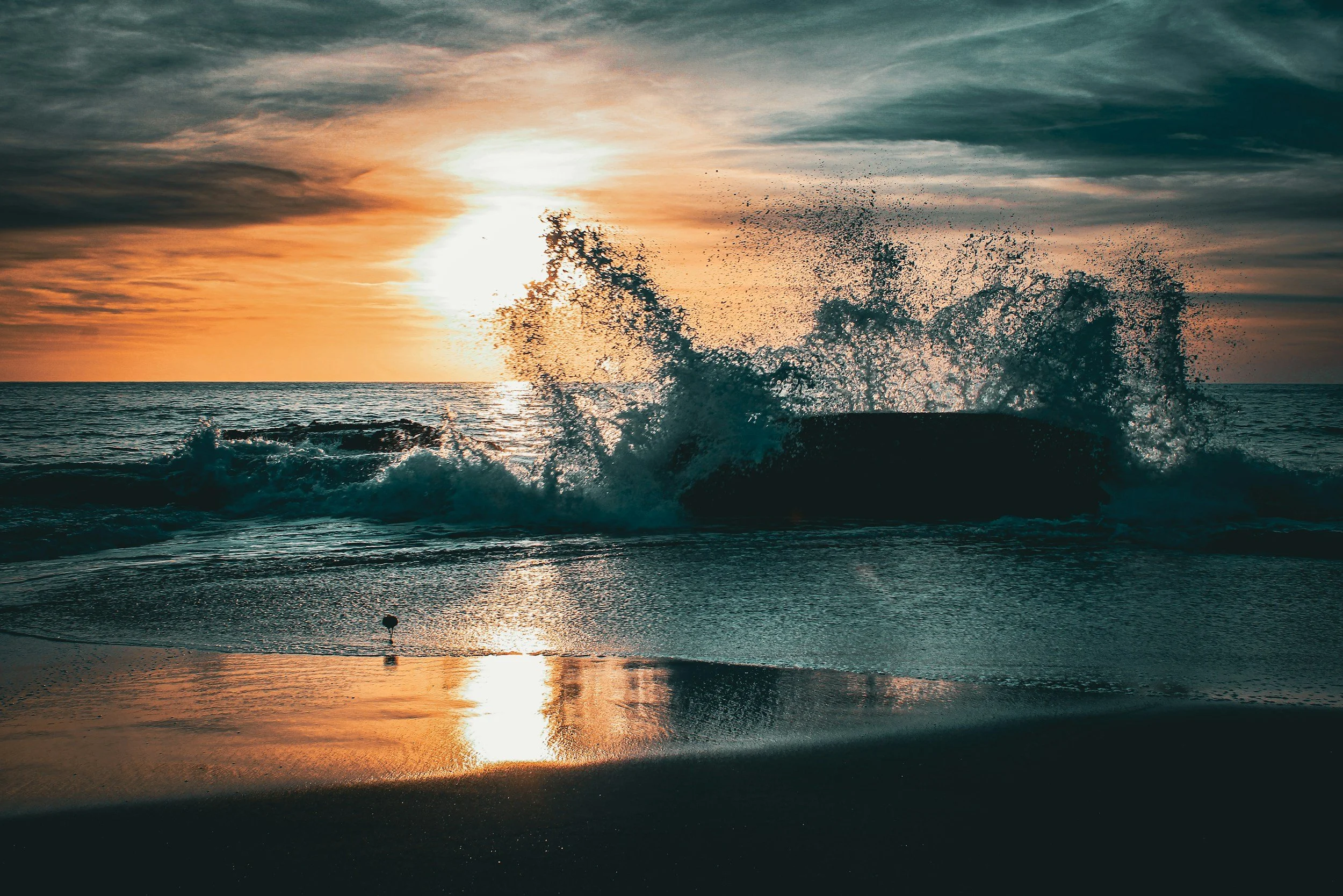 Una puesta de sol sobre el océano, con las olas rompiendo en la orilla, las nubes en el cielo y los reflejos en el agua.