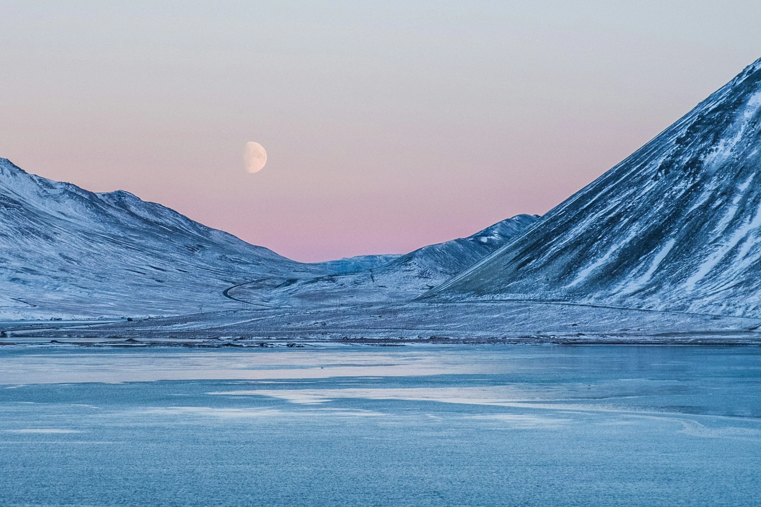 Snow-covered mountains under a light pink and blue sky with the moon visible in the background.