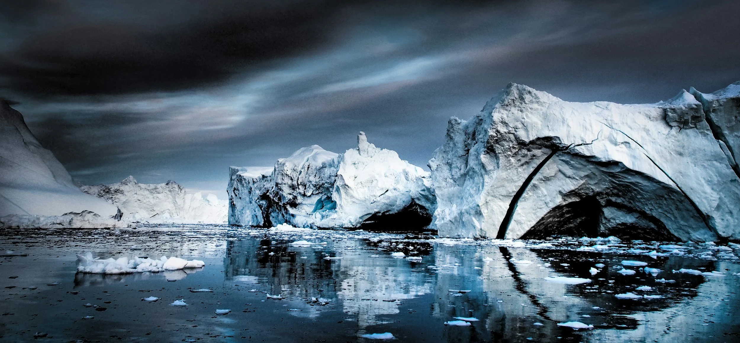 Icebergs floating in cold ocean water with dark cloudy sky overhead.