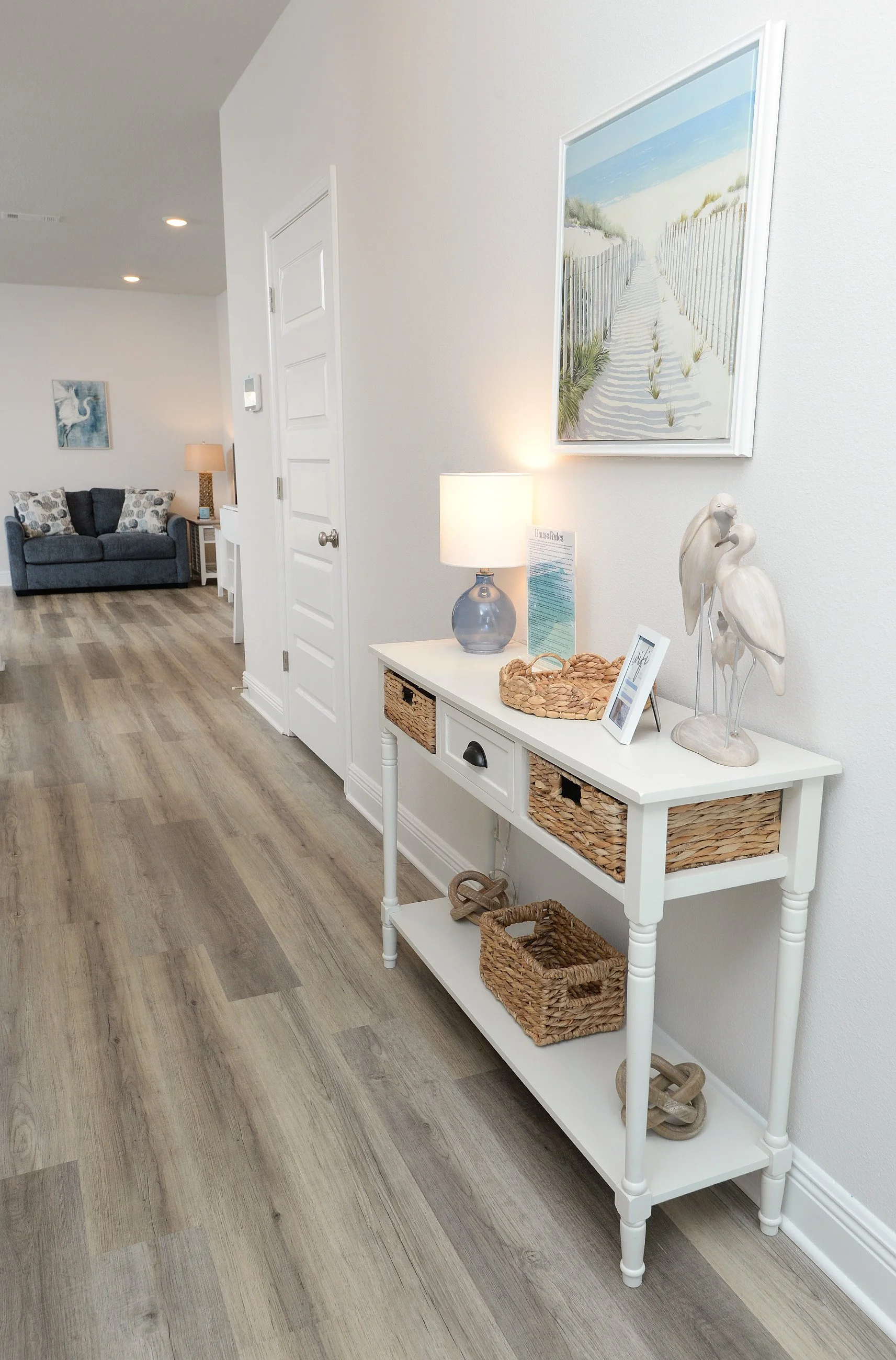 White console table with wicker baskets and decorative bird sculptures in a bright, coastal-themed home interior.