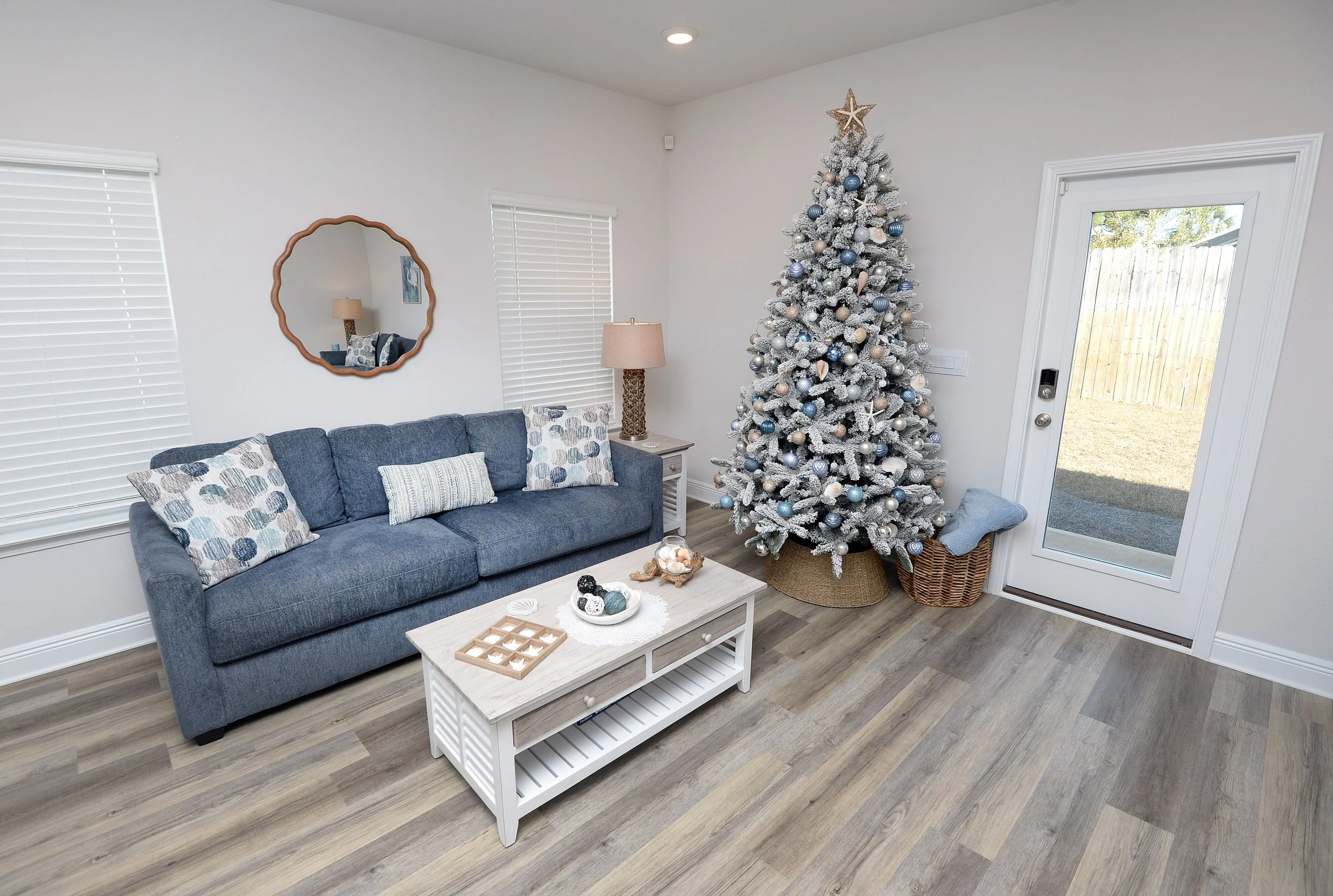Living room with blue sofa, white coffee table, holiday décor, and a decorated Christmas tree with blue, white, and silver ornaments.