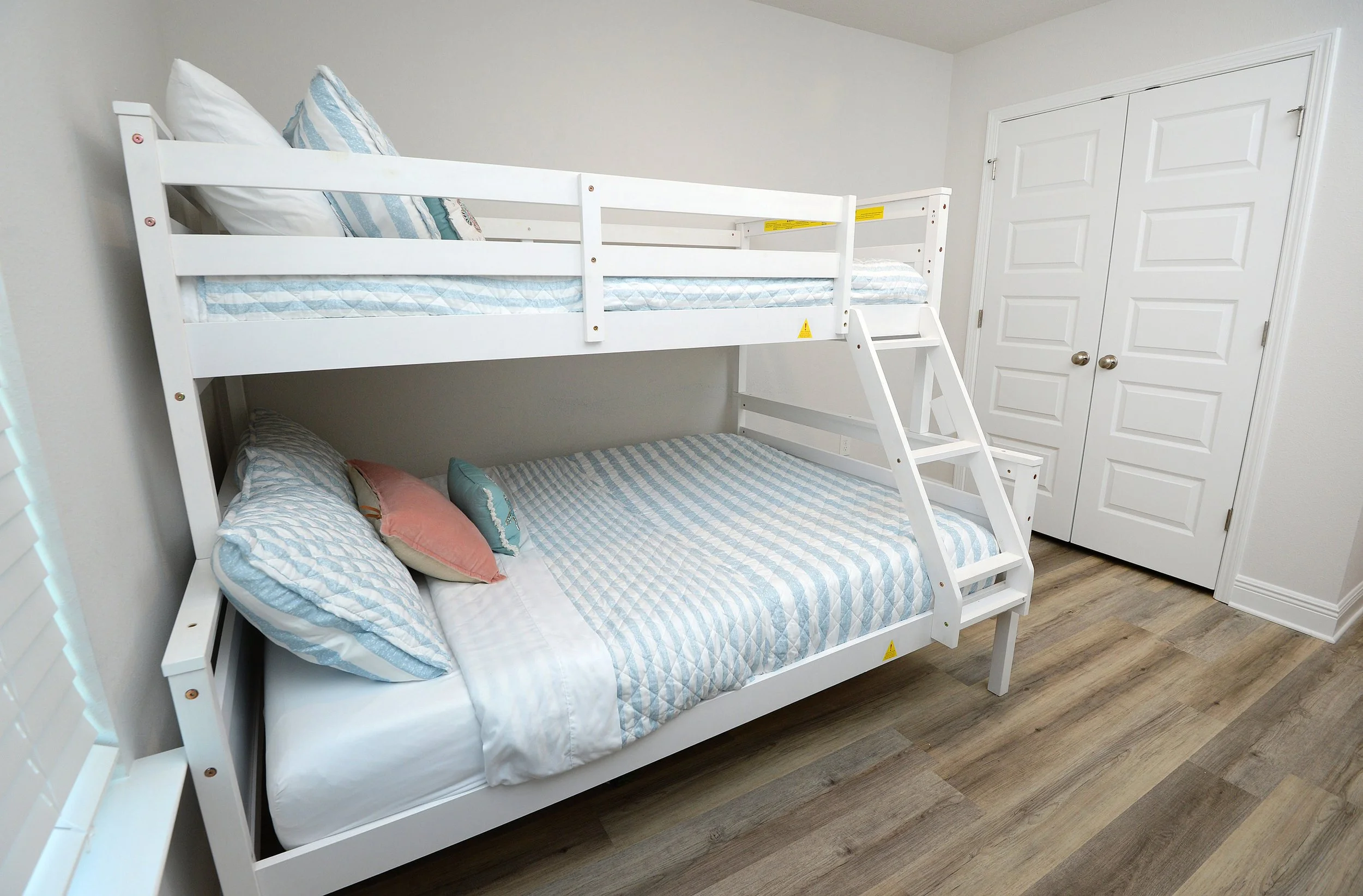 White bunk bed in a room with a closed closet door, with bed linens and pillows on both bunks.