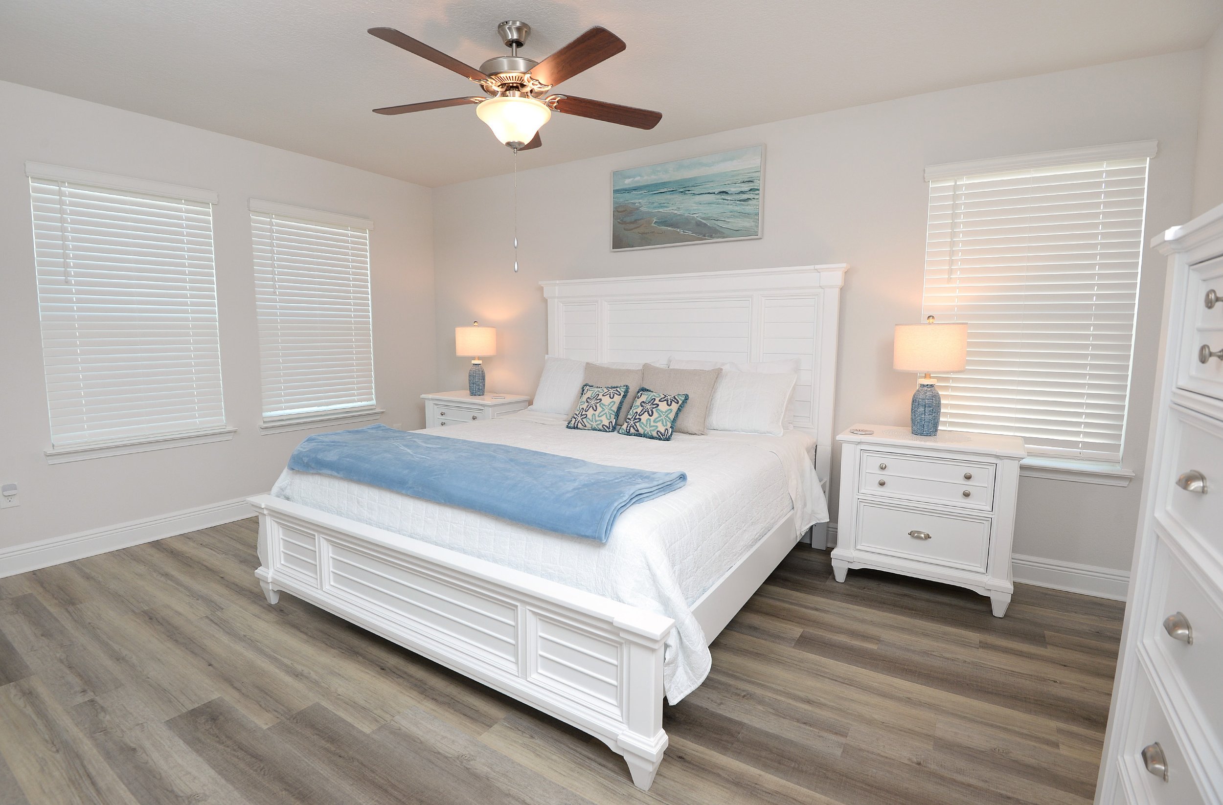 Spacious master bedroom at Coastal Tide Escapes vacation rental in Panama City Beach, featuring a king bed with white furniture, hardwood floors, and coastal beach decor