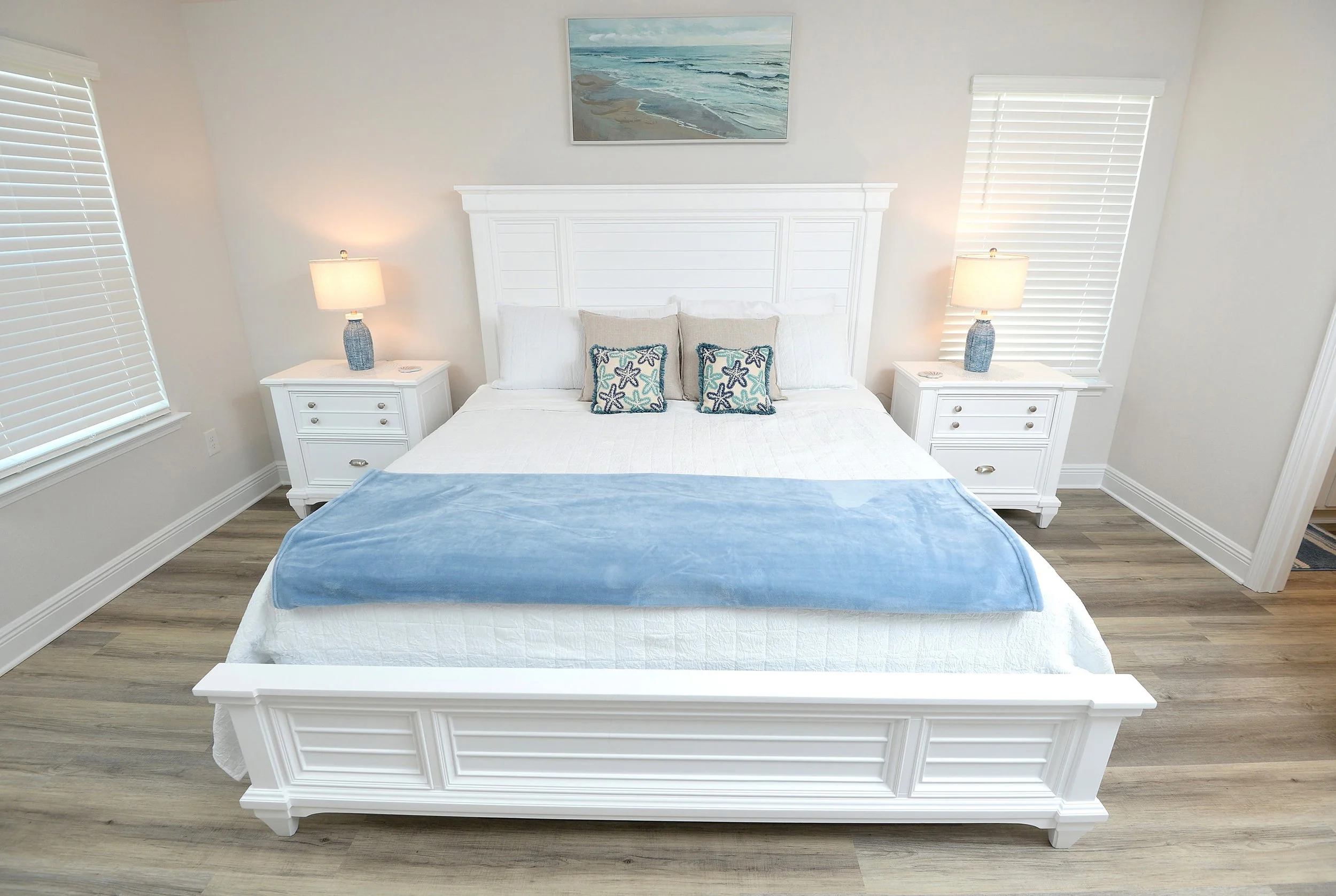 Master bedroom at Coastal Tide Escapes Panama City Beach vacation home, white coastal bedroom furniture with blue accent pillows and beach wall art