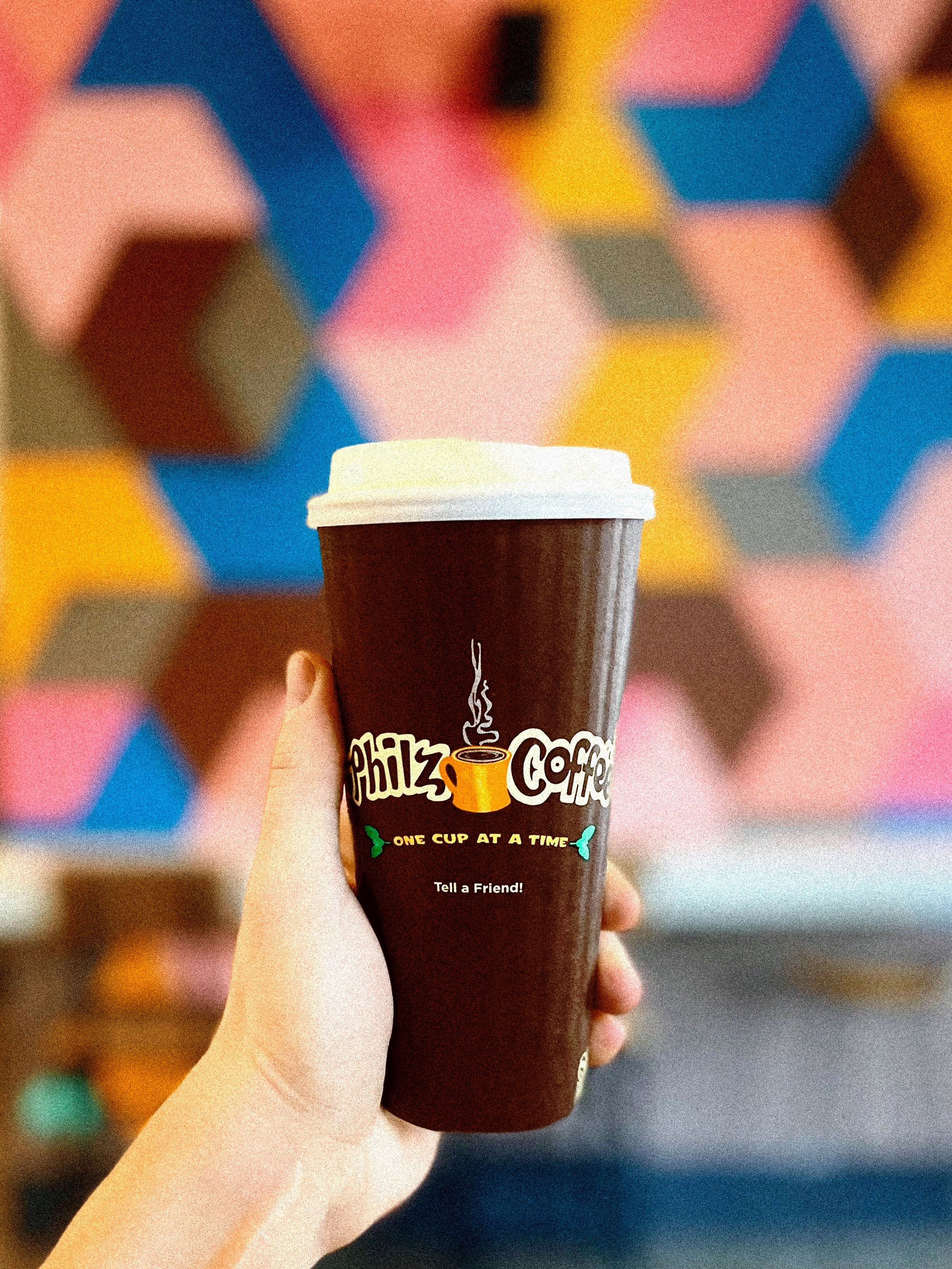 Philz Coffee cup held in front of Andrew Haan’s colorful geometric mural in Downtown Los Angeles.