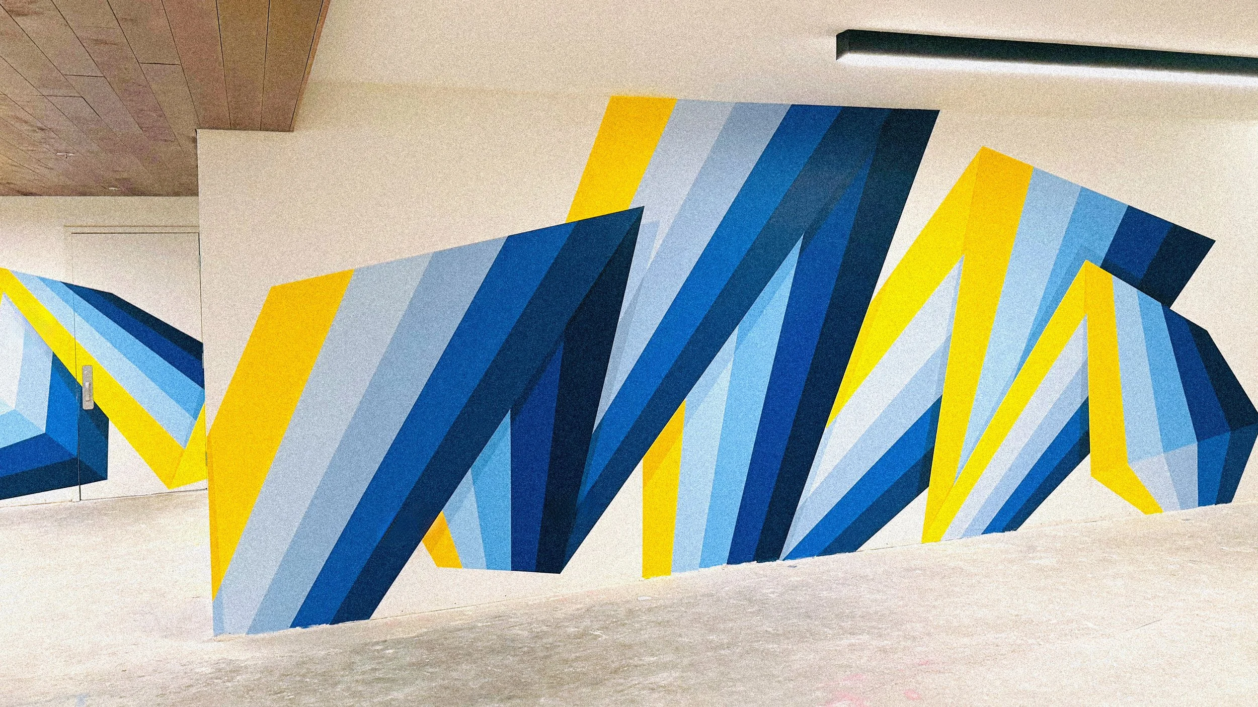Close-up of the UCLA mural showing layered blue, yellow and white geometric forms by Andrew Haan.
