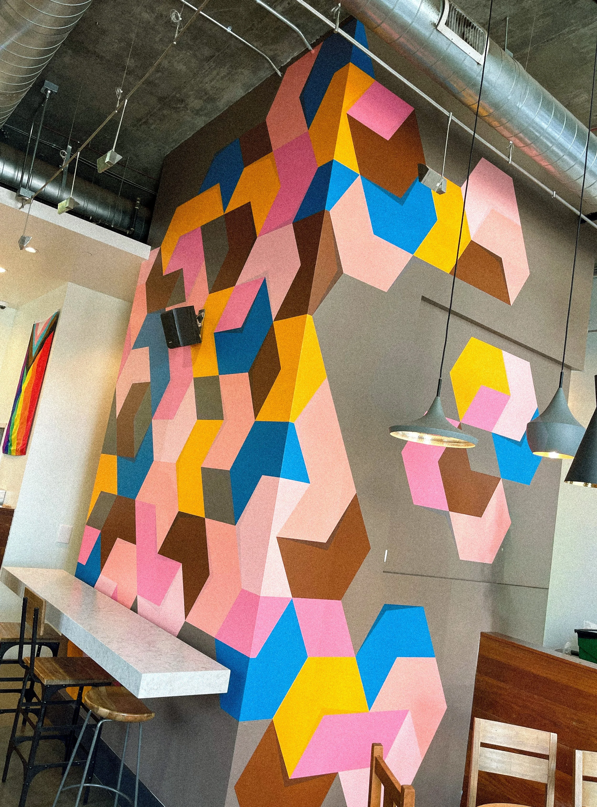 Angled interior view of Andrew Haan’s colorful geometric mural wrapping the wall at Philz Coffee.