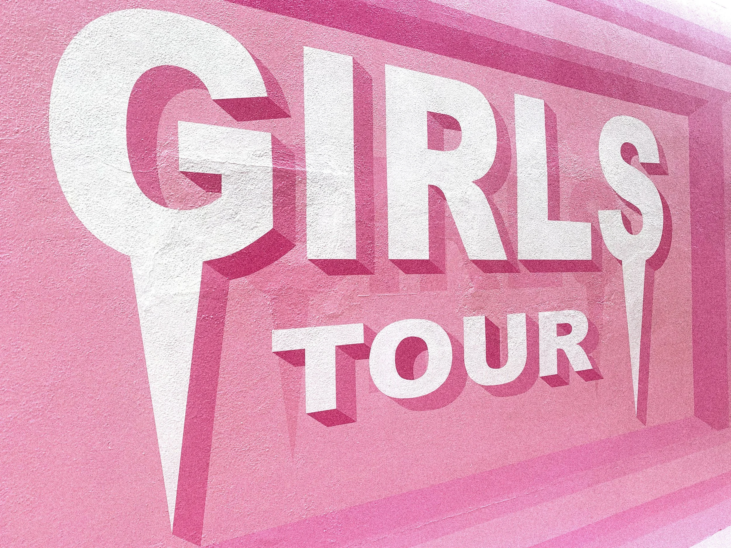 Close-up of the Girls Tour mural showing dimensional white lettering and layered shades of pink.