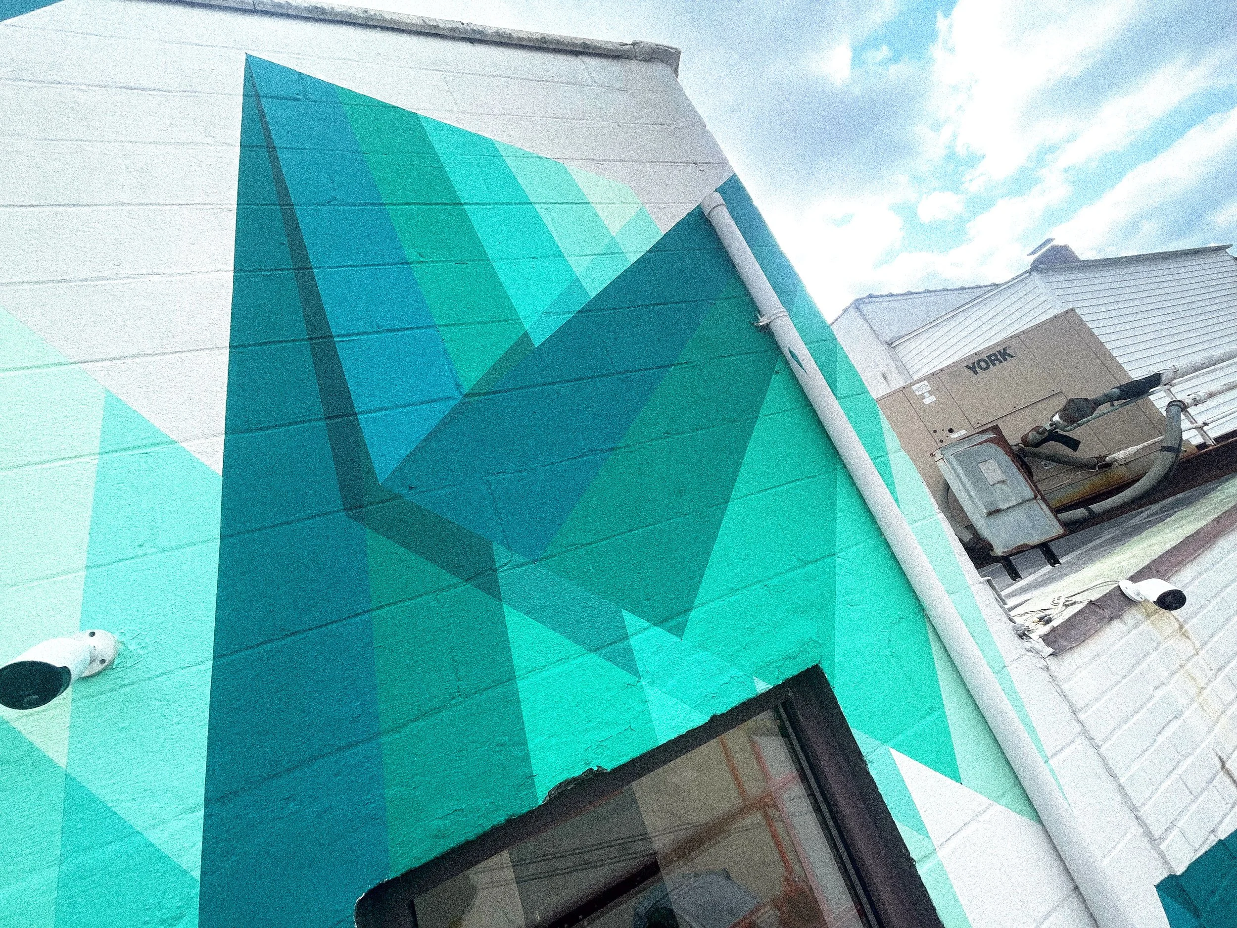 Teal and green geometric forms wrapping the architecture of the Broome County public art mural