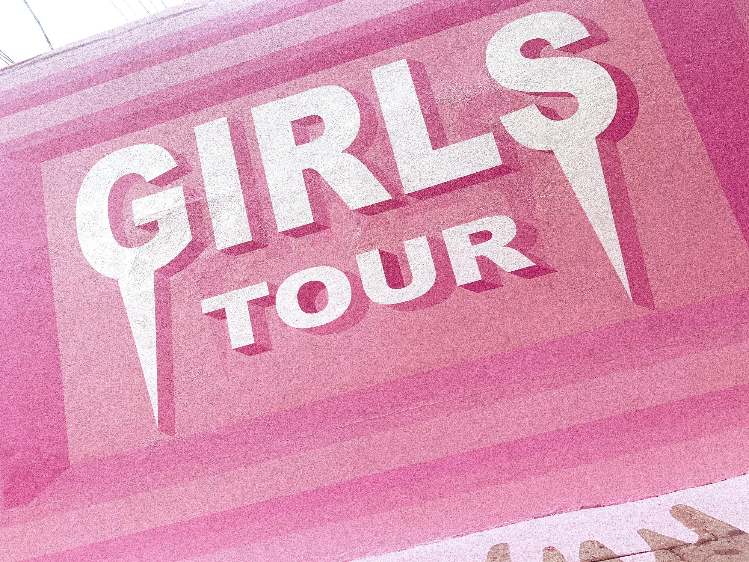 Angled detail of the finished Girls Tour mural in West Hollywood featuring oversized lettering and geometric pink bands.