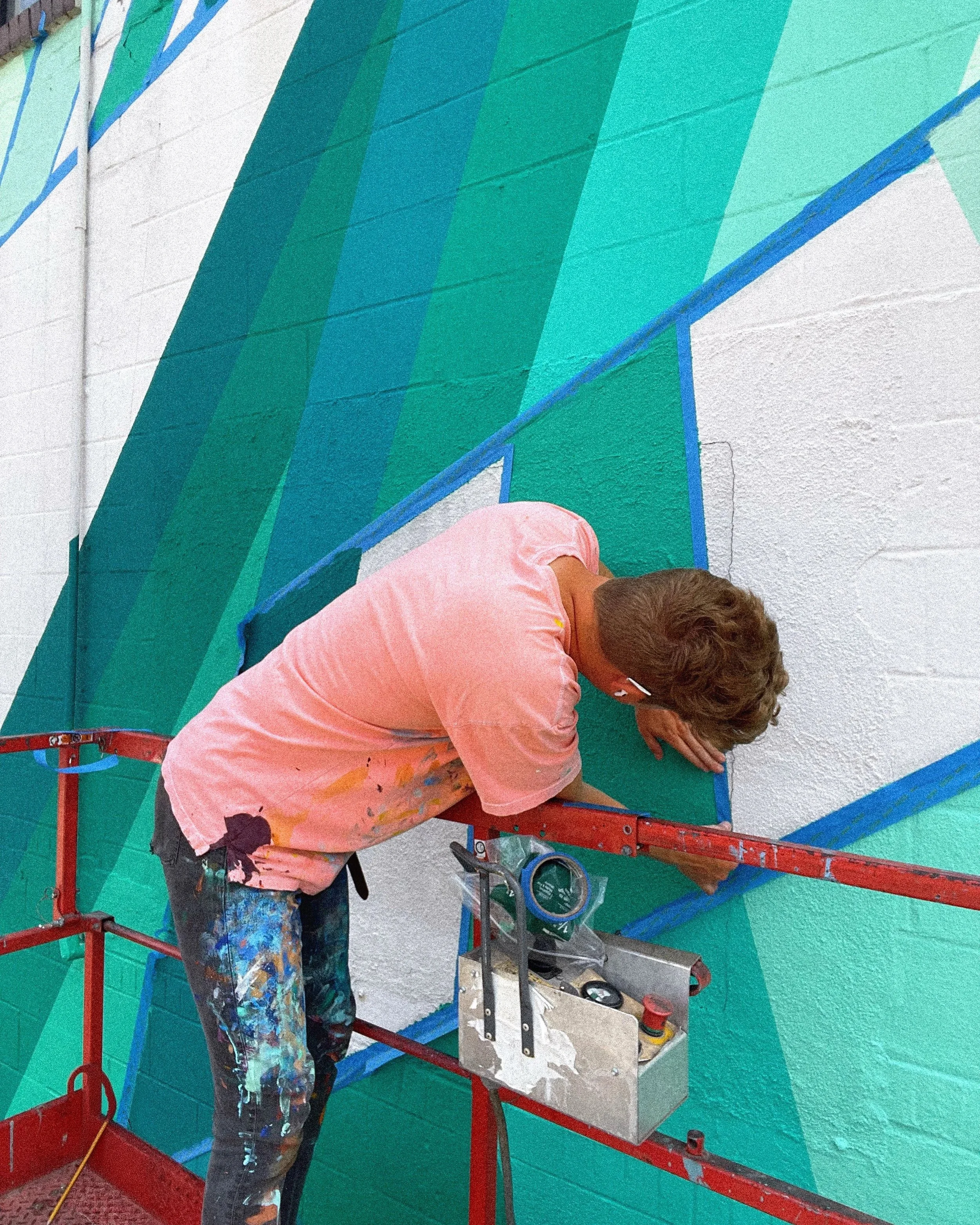 Andrew Haan painting the geometric Broome County mural from a lift in Endicott, New York