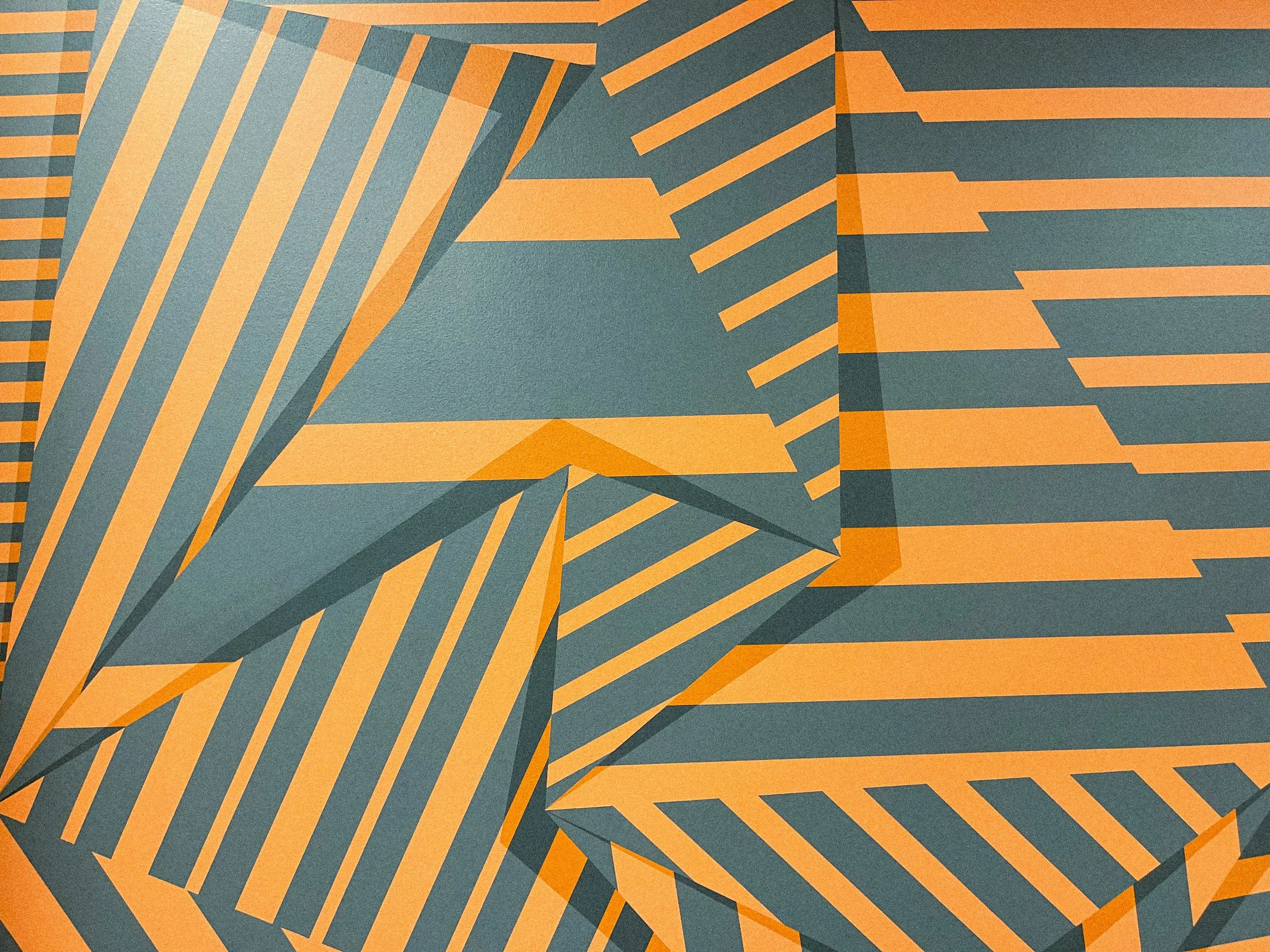 Detailed view of the Laguna office mural showing shifting perspective and interlocking orange and charcoal geometric forms.