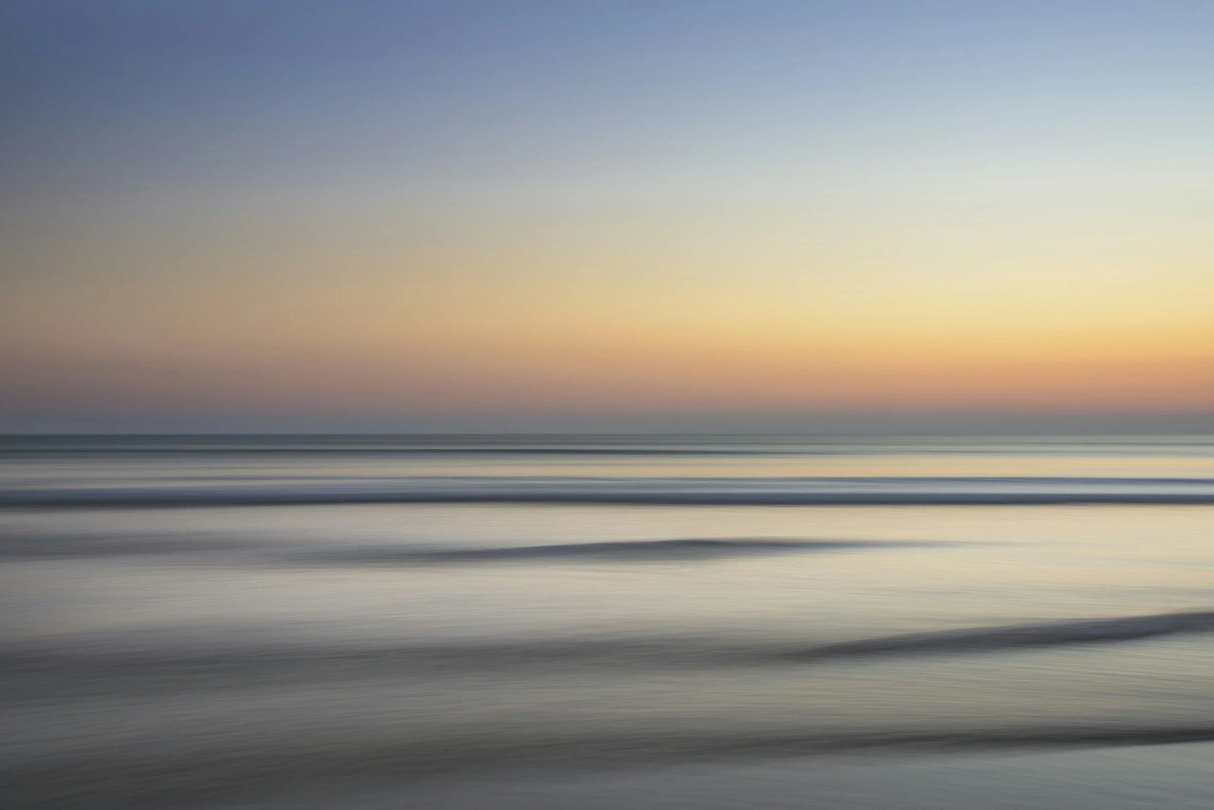 The blue and orange horizon at sunset across a calm sea with little waves.