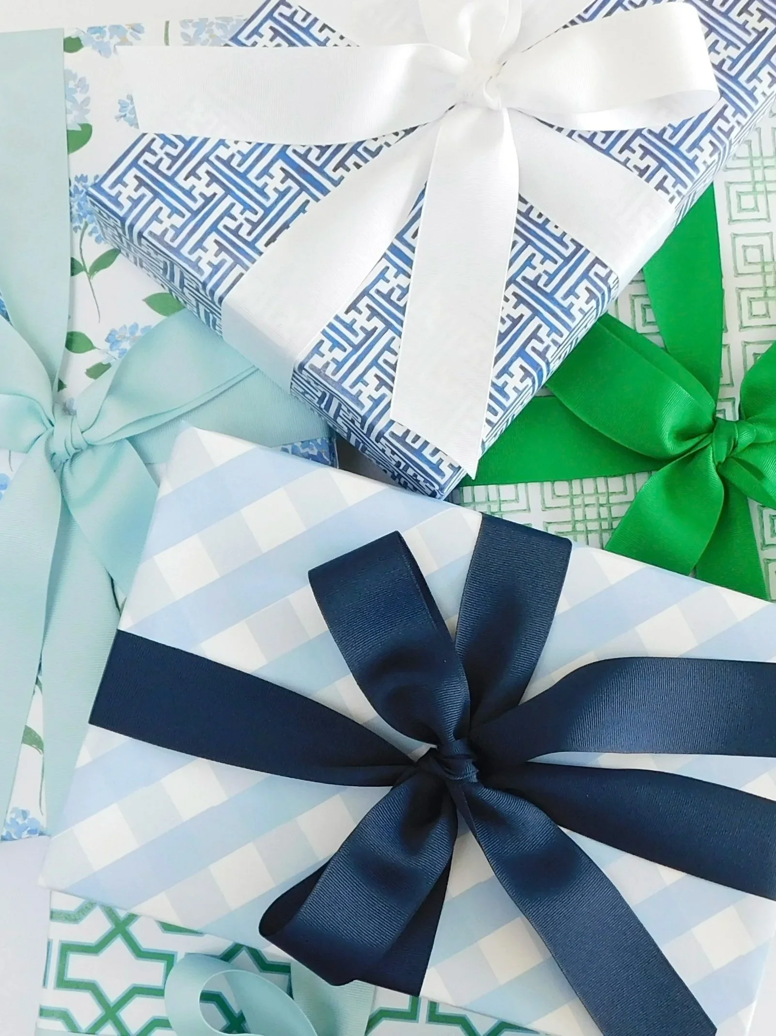 Close-up of wrapped gift boxes with decorative bows, one in navy blue with a bow, and others in pastel colors with bows, on a patterned paper background.