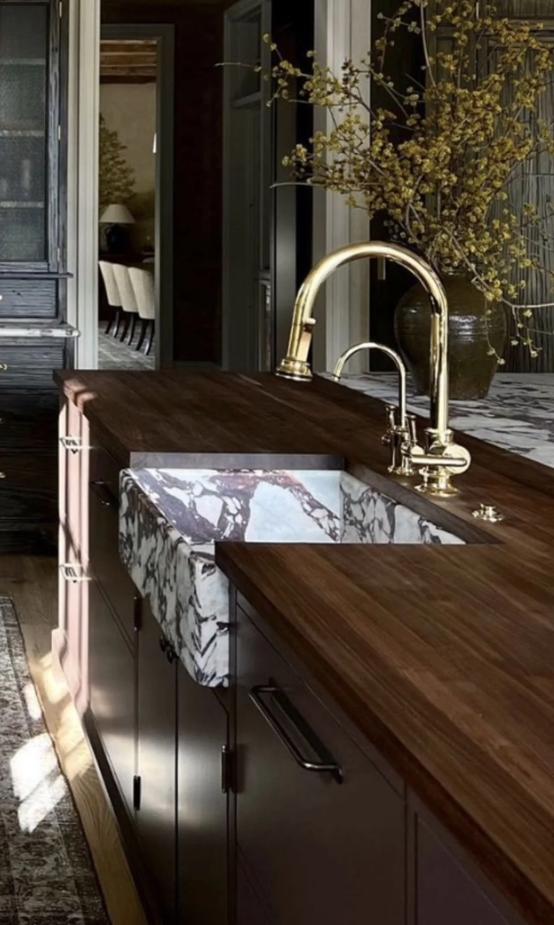Kitchen island with a wooden countertop, marble sink, gold faucet, and a large vase with yellow flowers in the background.