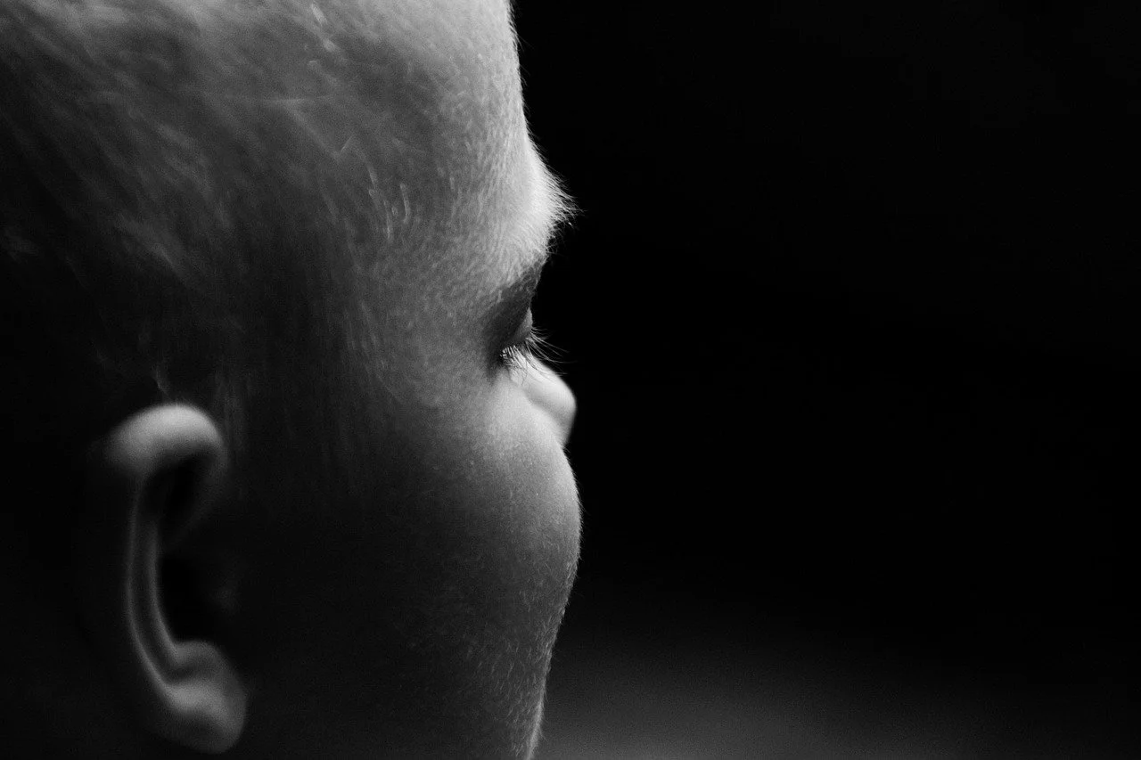 Black-and-white side profile of a young child looking into a dark empty space