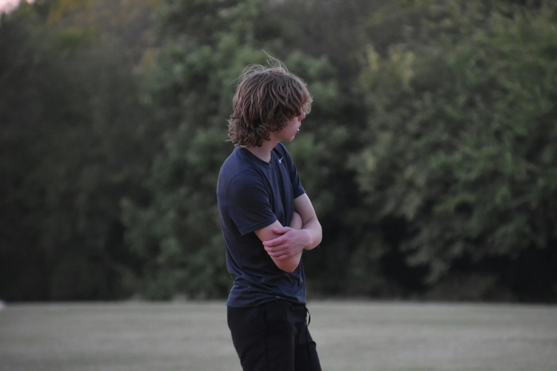 Young person standing in a field with arms crossed while looking off into the distance